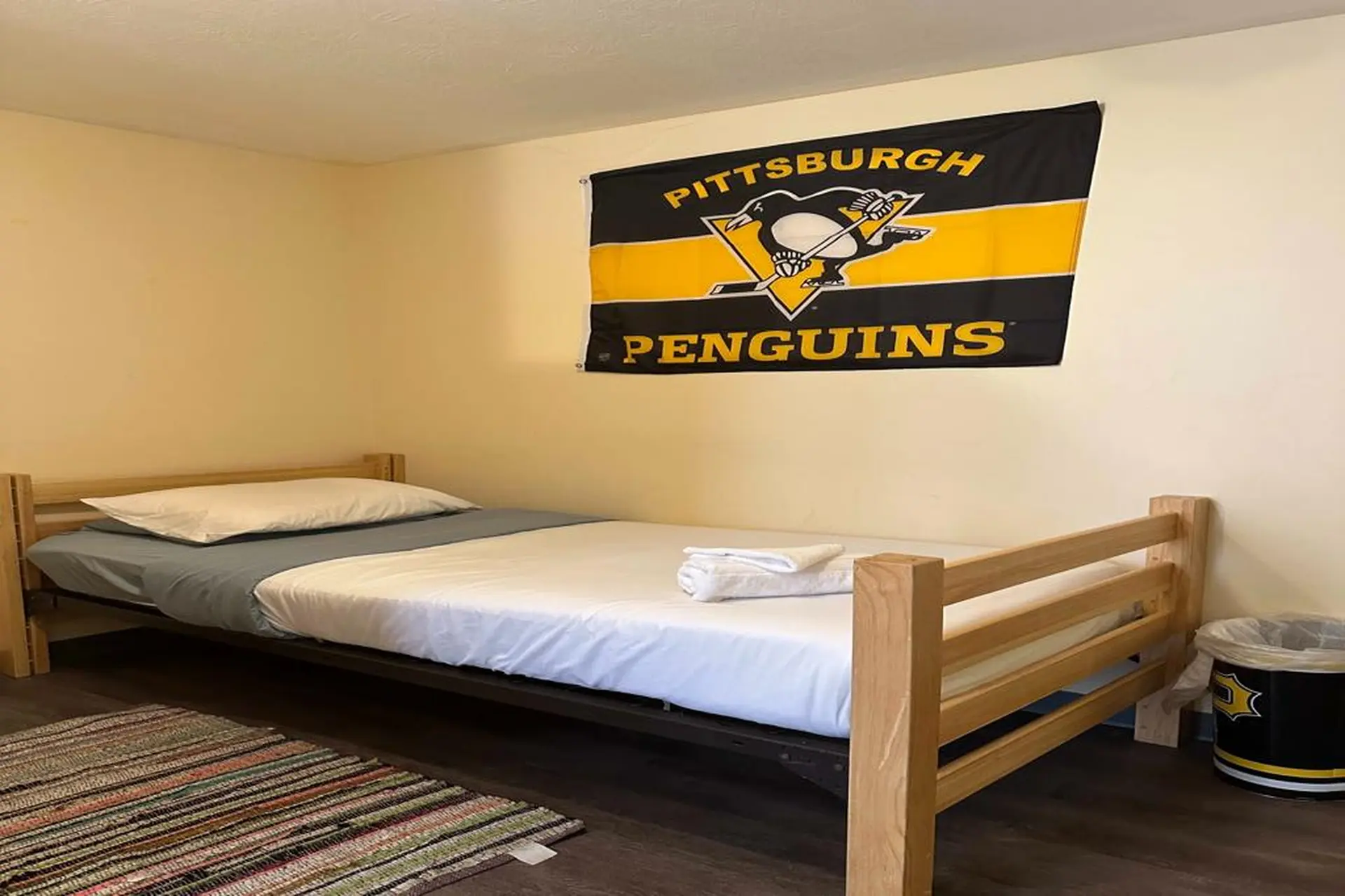 A bedroom with a Pittsburgh Penguins flag above a twin bed.