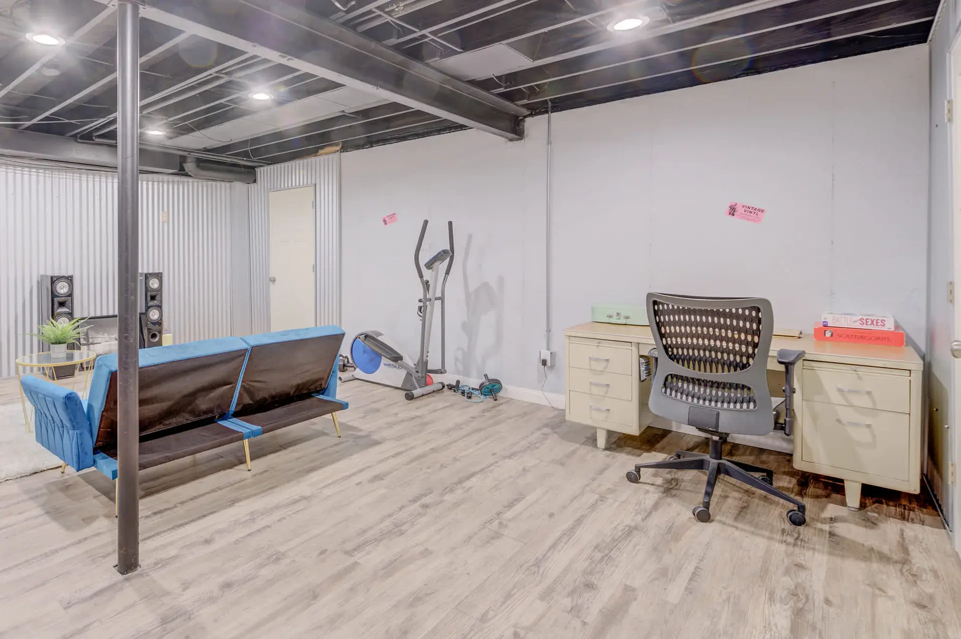 A basement room with a blue sofa, exercise equipment, and a desk with a chair.