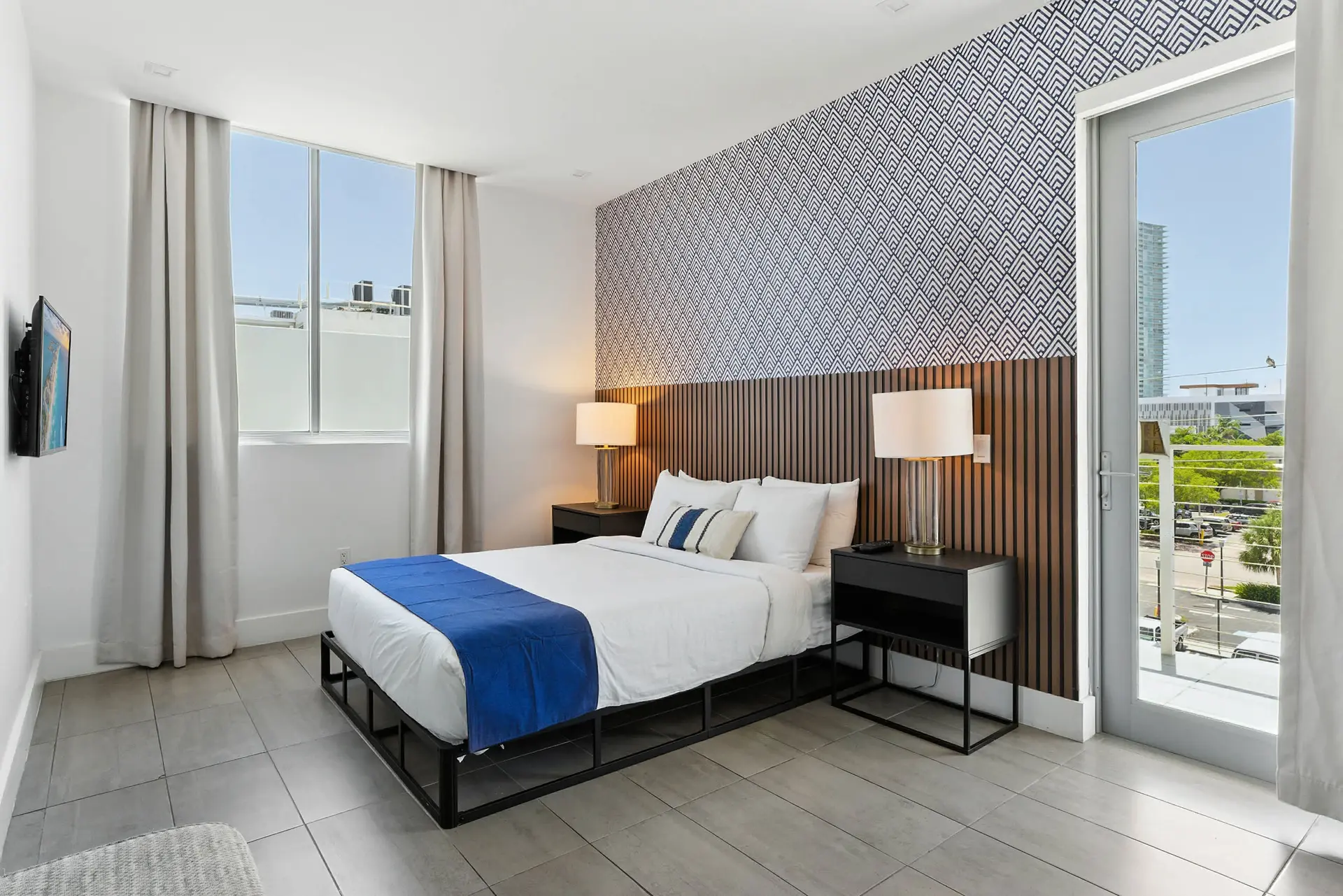 Modern bedroom with a large window, bed, and patterned wallpaper.