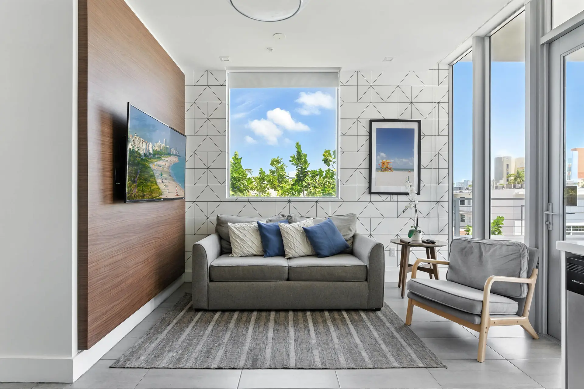A grey sofa sits on a striped rug in a modern living room with a wall of windows.