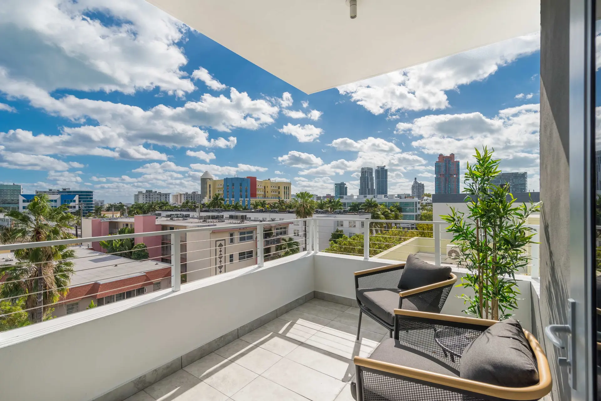 A balcony with two chairs overlooking a cityscape under a blue sky with white clouds.