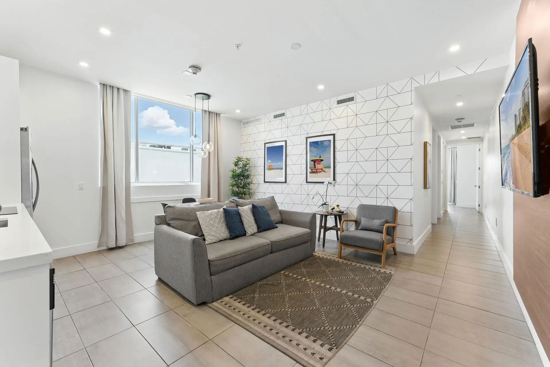 A living room with a grey sofa, armchair, and geometric wallpaper.