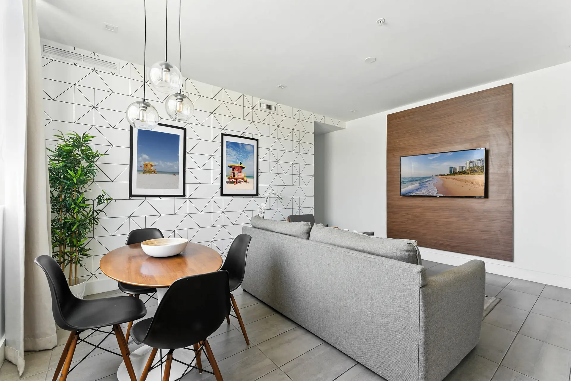 A modern living room with a grey sofa, wood accent wall with TV, and dining area.