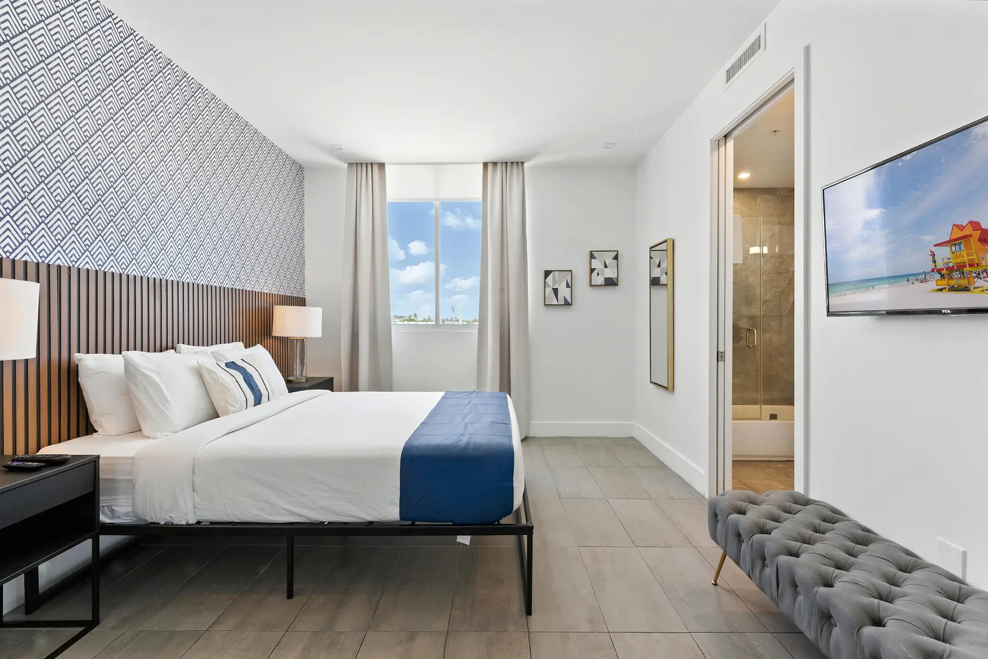 A modern bedroom with a king-size bed, blue and white patterned wallpaper, and a TV.
