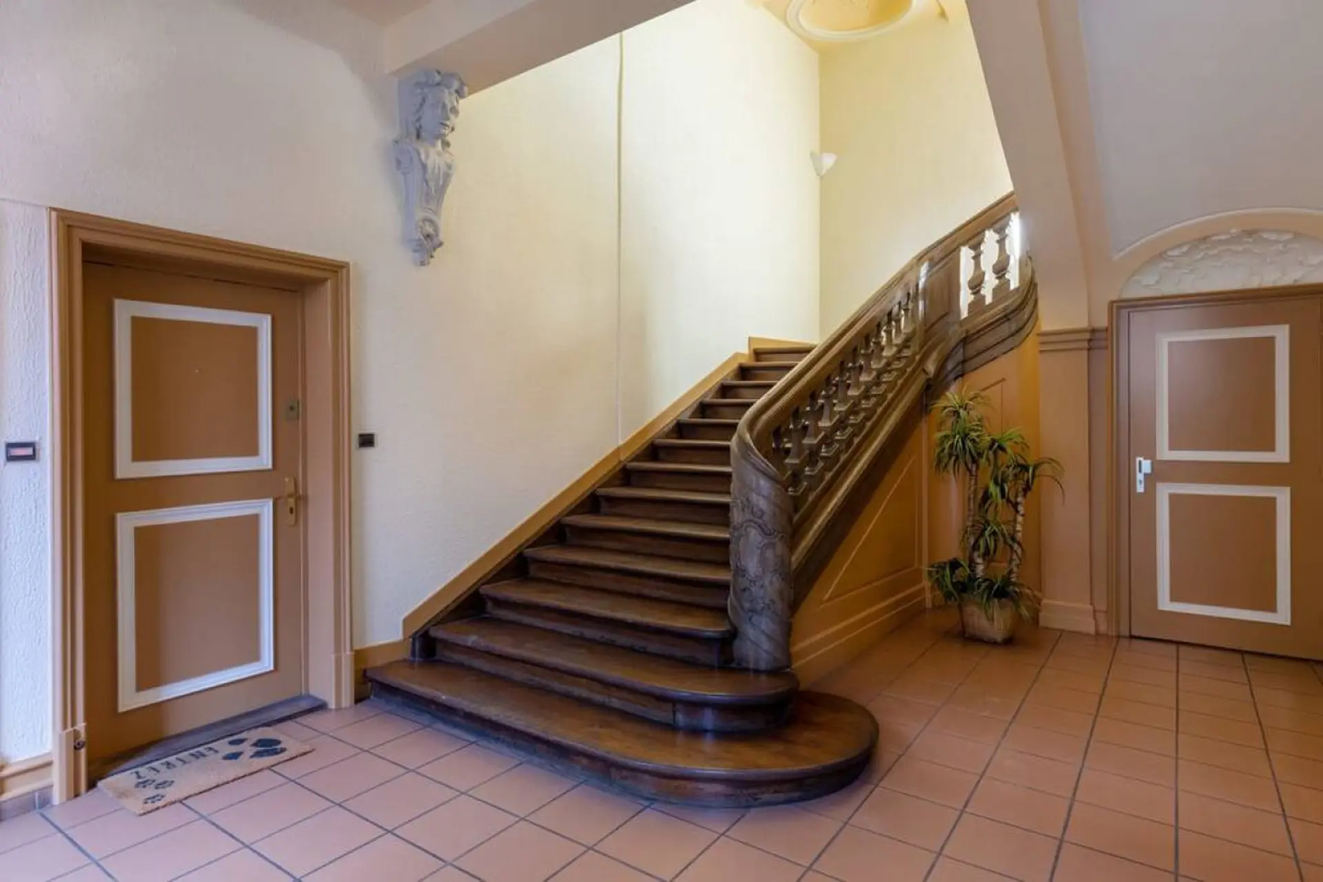 A wooden staircase with carved details and a marble newel post, flanked by two doors.