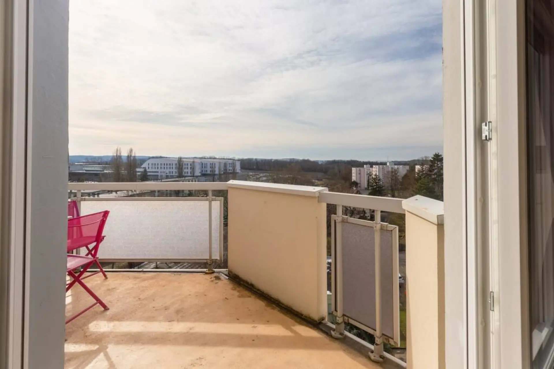 View of a balcony with chairs overlooking buildings and trees.