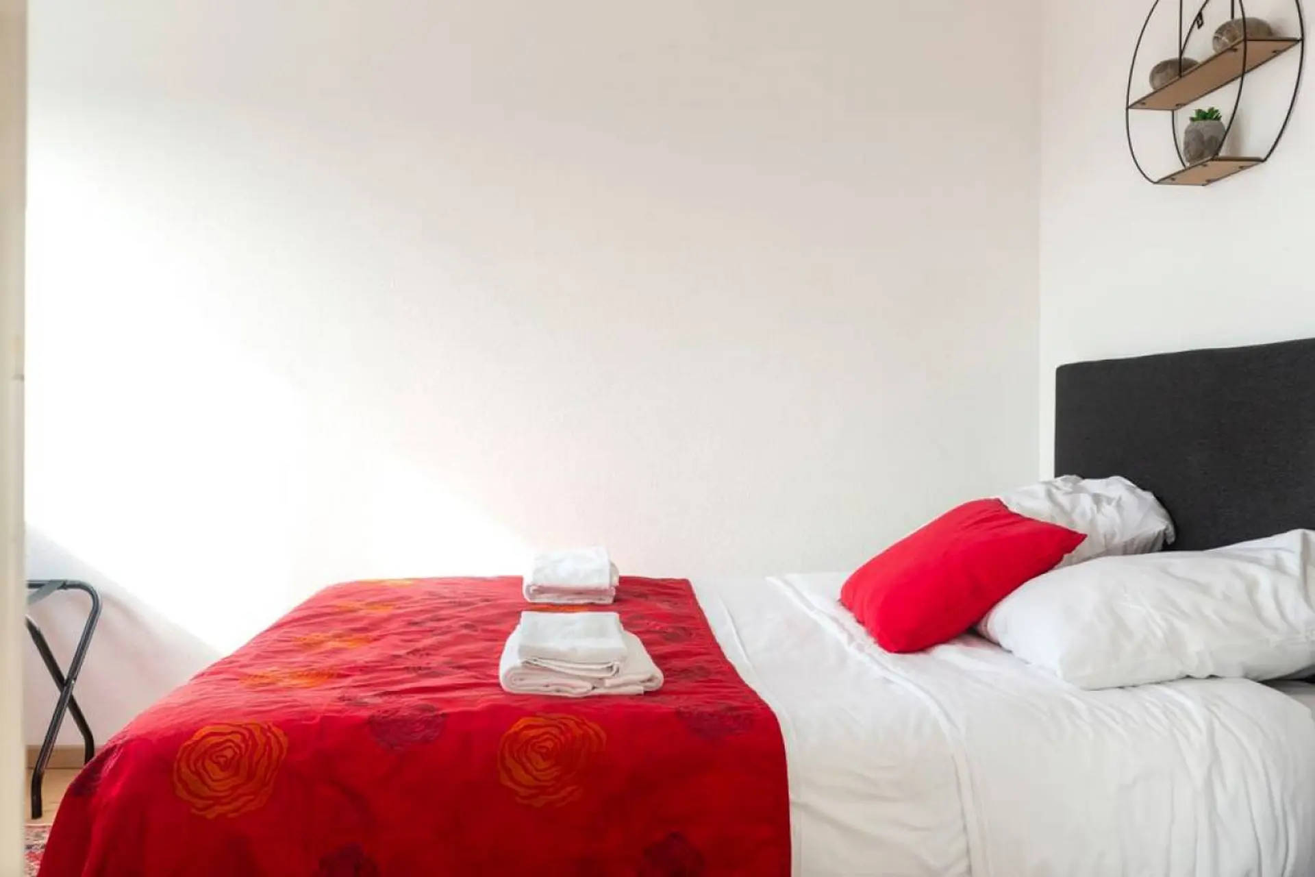 A bed with red floral sheets and white towels, a red pillow, and a dark headboard.