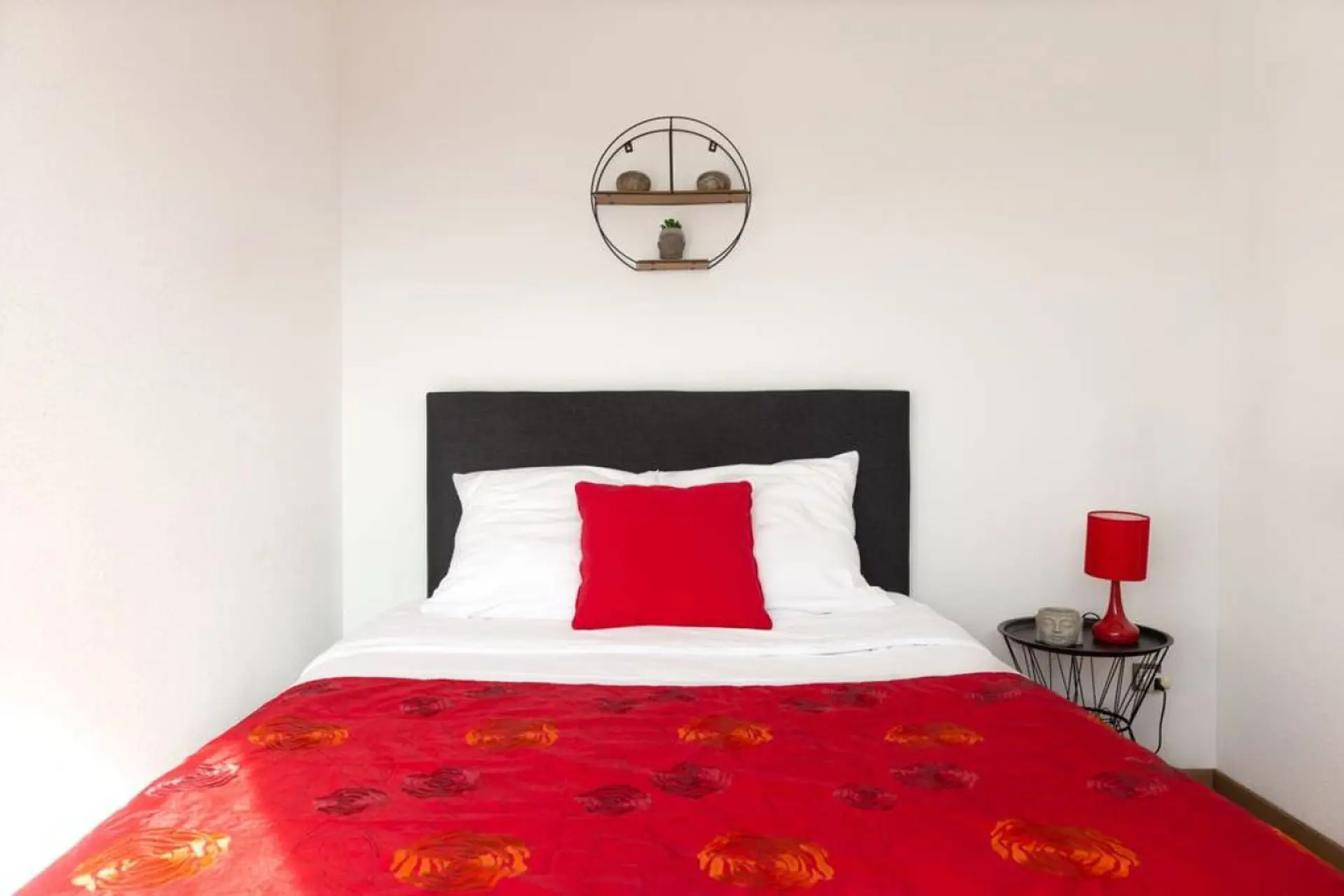 A bedroom with a red bedspread, white pillows, and a red lamp.