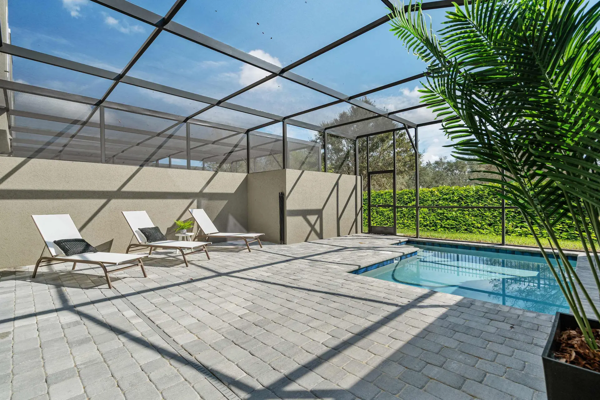 A screened-in patio with lounge chairs and a swimming pool.