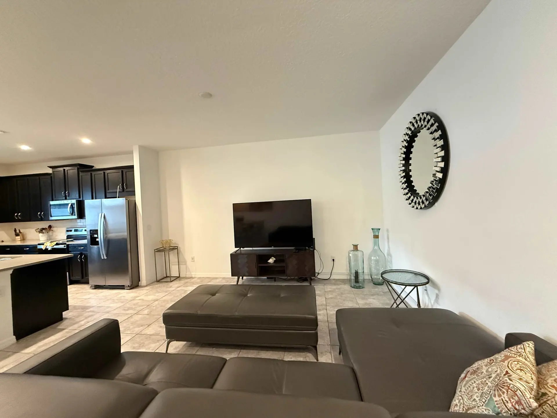 A modern living room and kitchen area with dark cabinetry, stainless steel appliances, and a section