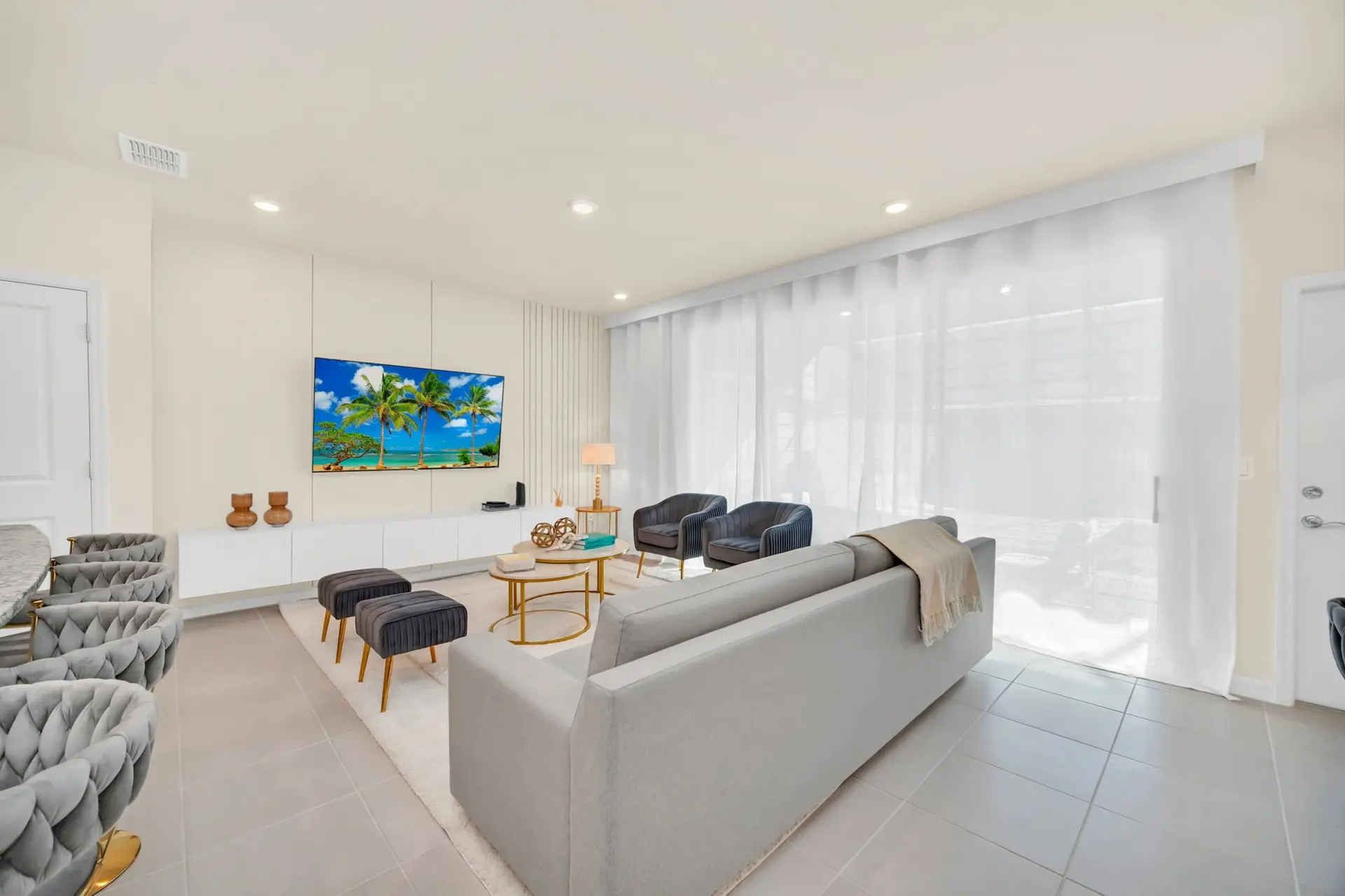A bright living room with a grey sofa, plush chairs, and a TV.
