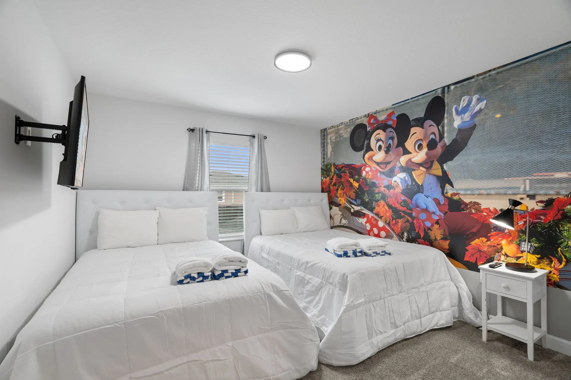 A bedroom with two beds, Mickey and Minnie Mouse mural, and a mounted TV.
