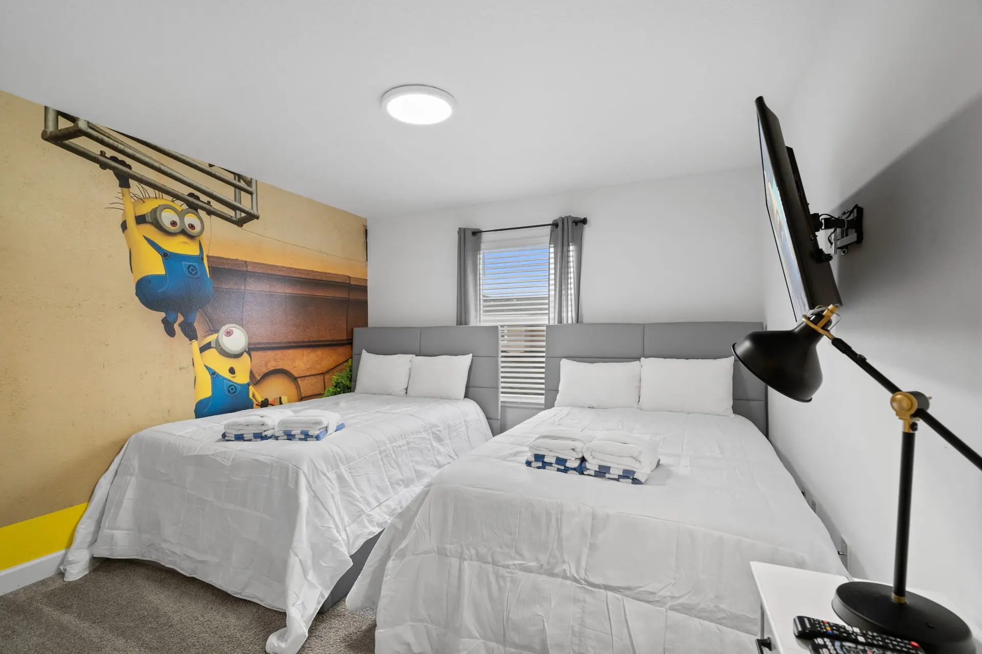 A bedroom with two beds, Minions wallpaper, and a TV.