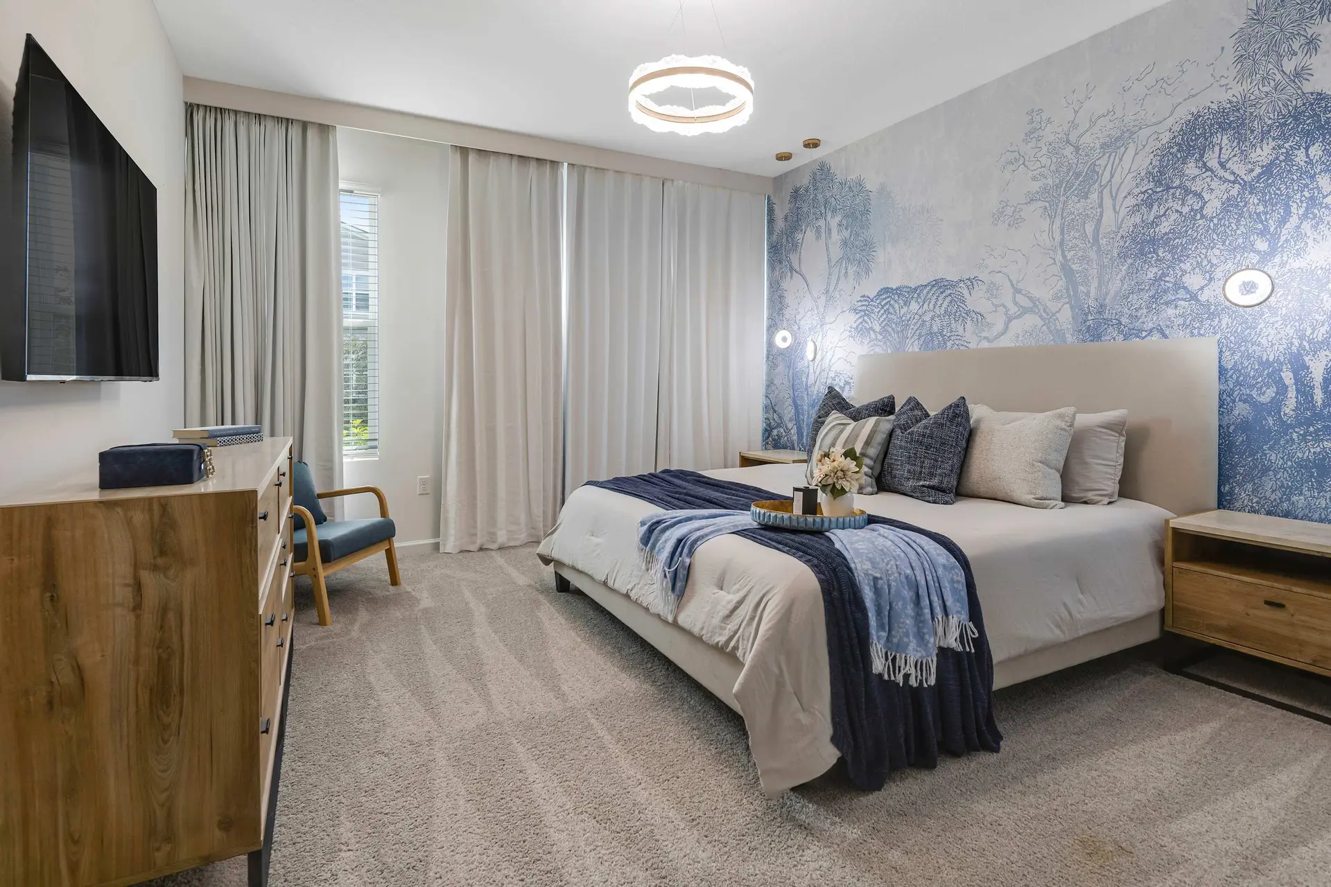 A luxurious bedroom with a king-size bed, blue and white tree-themed wallpaper, and a large window w