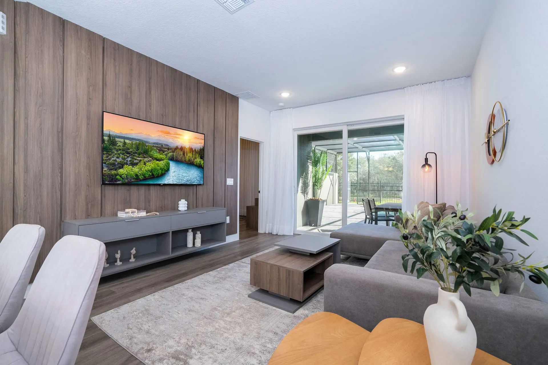 A living room features a TV on a wooden wall, a grey couch, and a sliding glass door leading outside