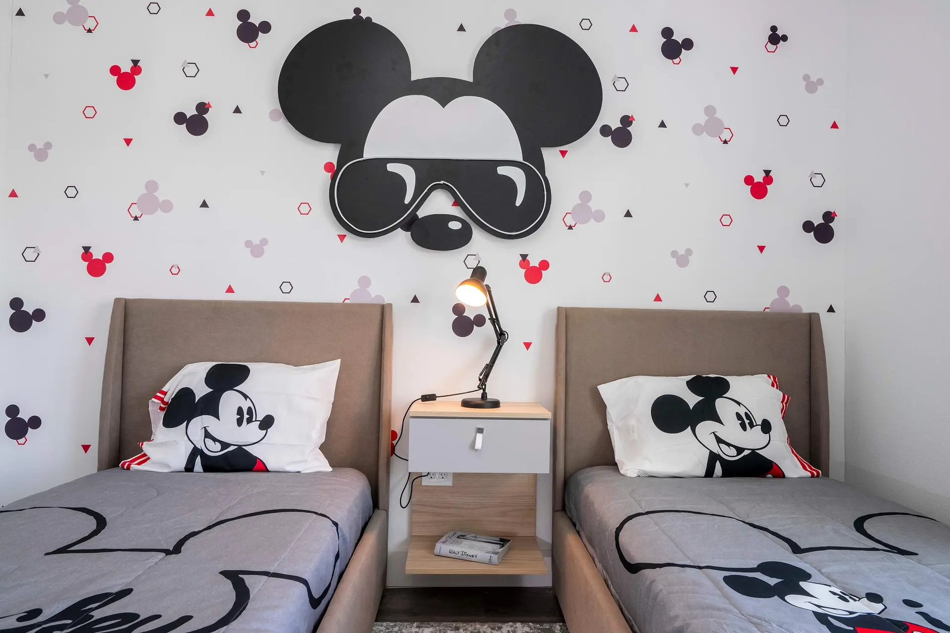 Two beds with Mickey Mouse decor, a large Mickey Mouse cutout on the wall, and a bedside table.