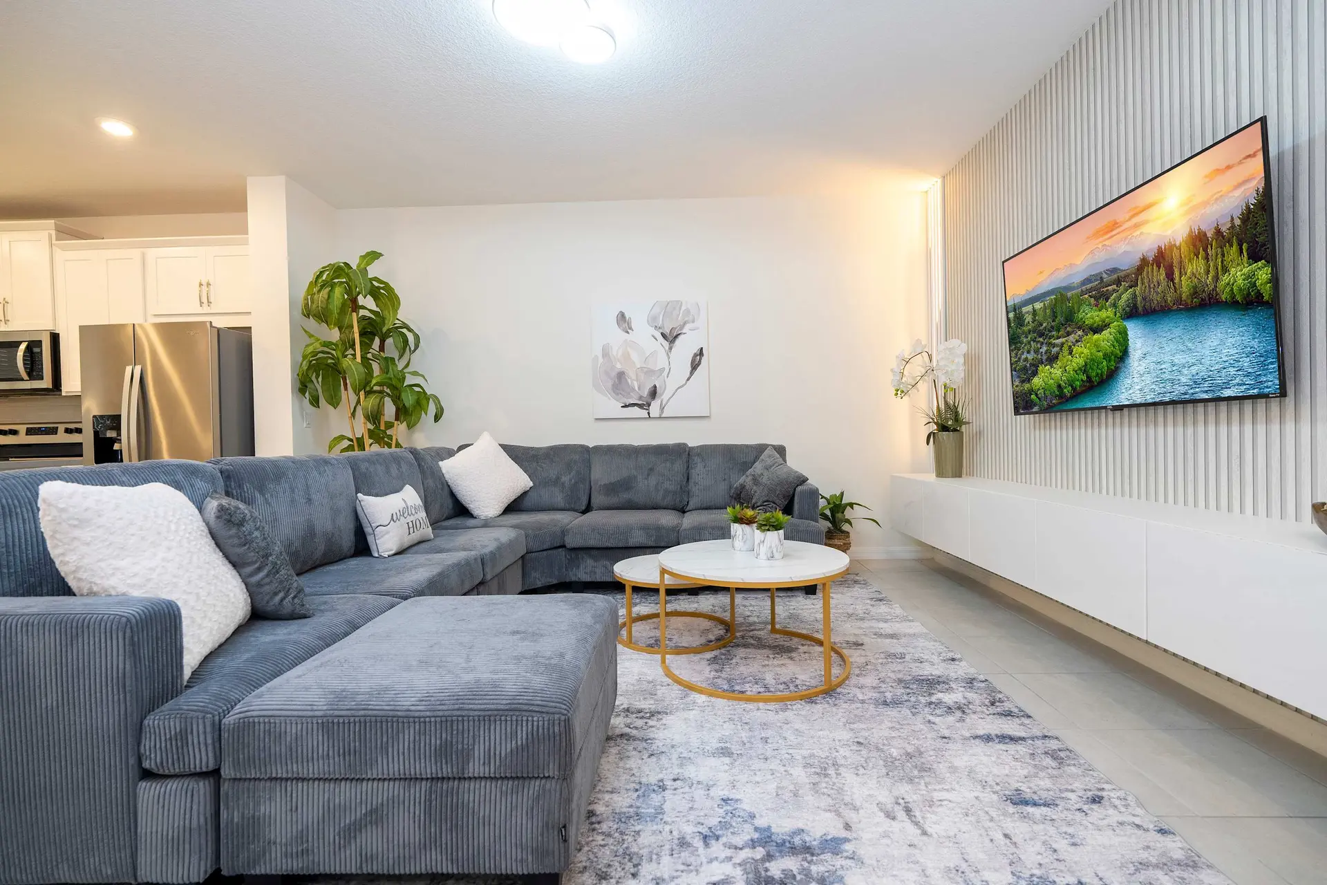 A spacious living room with a gray sectional sofa, a marble coffee table, and a wall-mounted TV disp