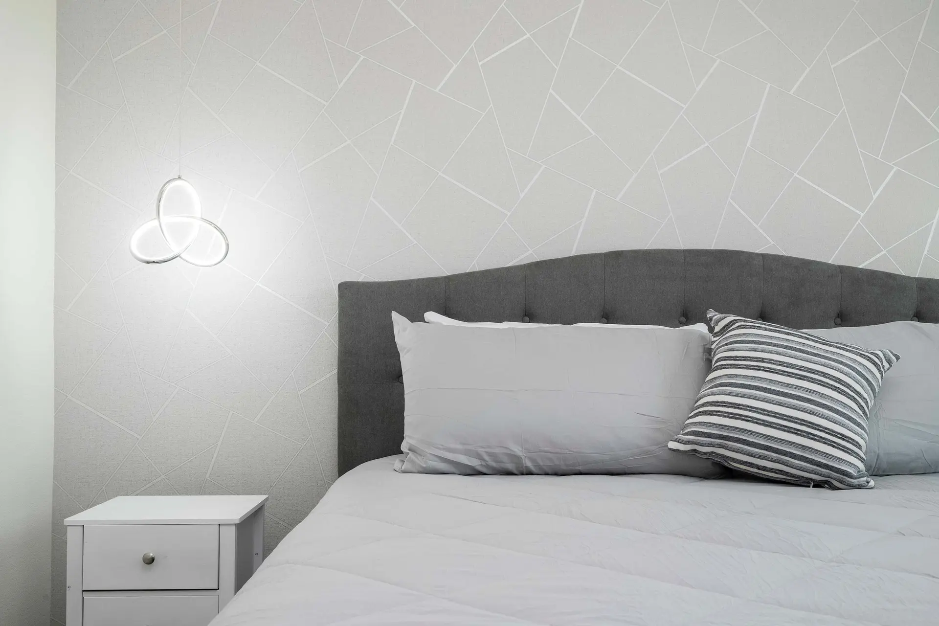 A close-up of a bed with a grey upholstered headboard and white bedding.