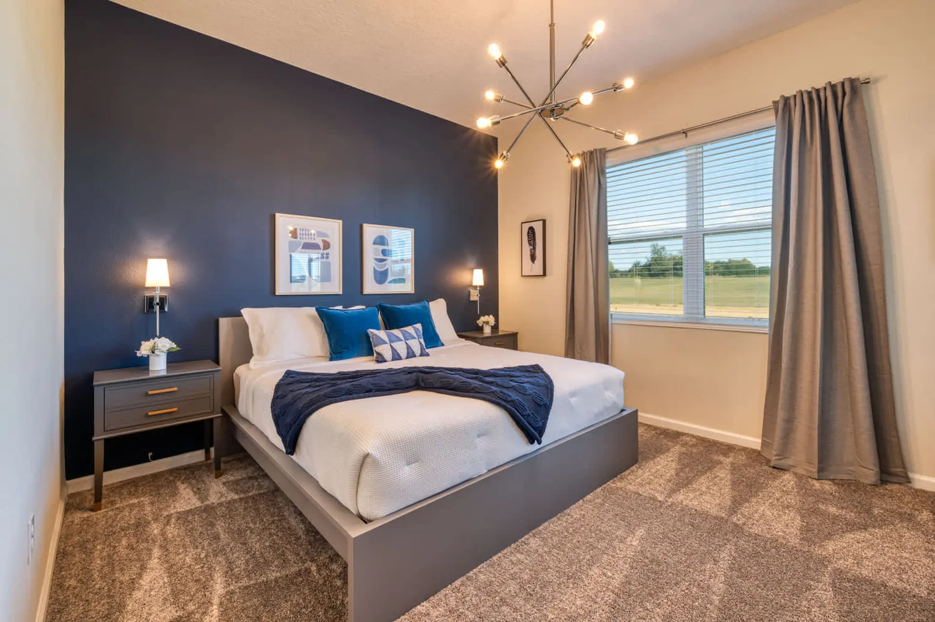 A modern bedroom with a king-size bed, navy blue accent wall, and a Sputnik chandelier.