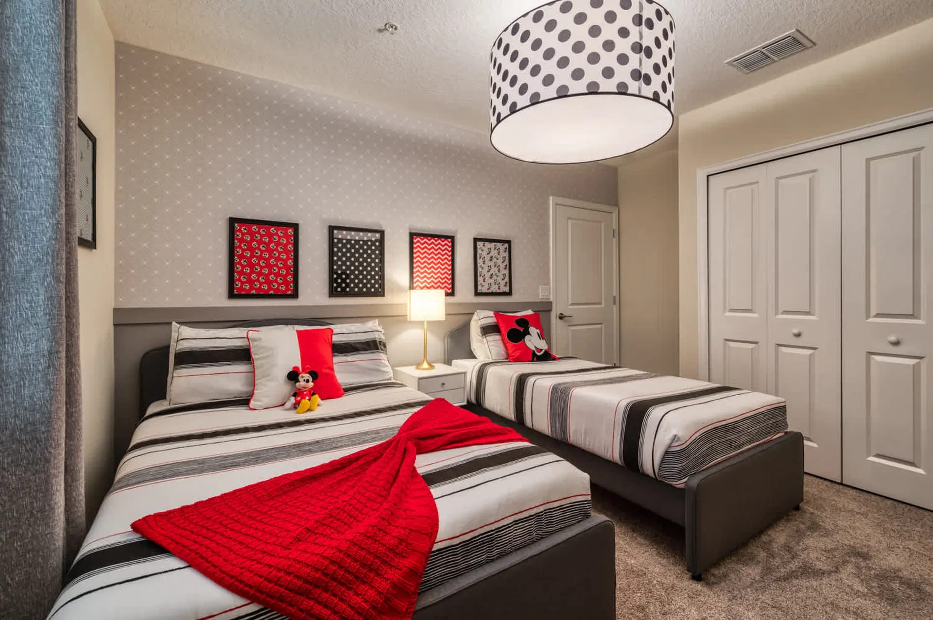 Mickey Mouse themed bedroom with two beds, patterned wallpaper and polka dot lampshade.