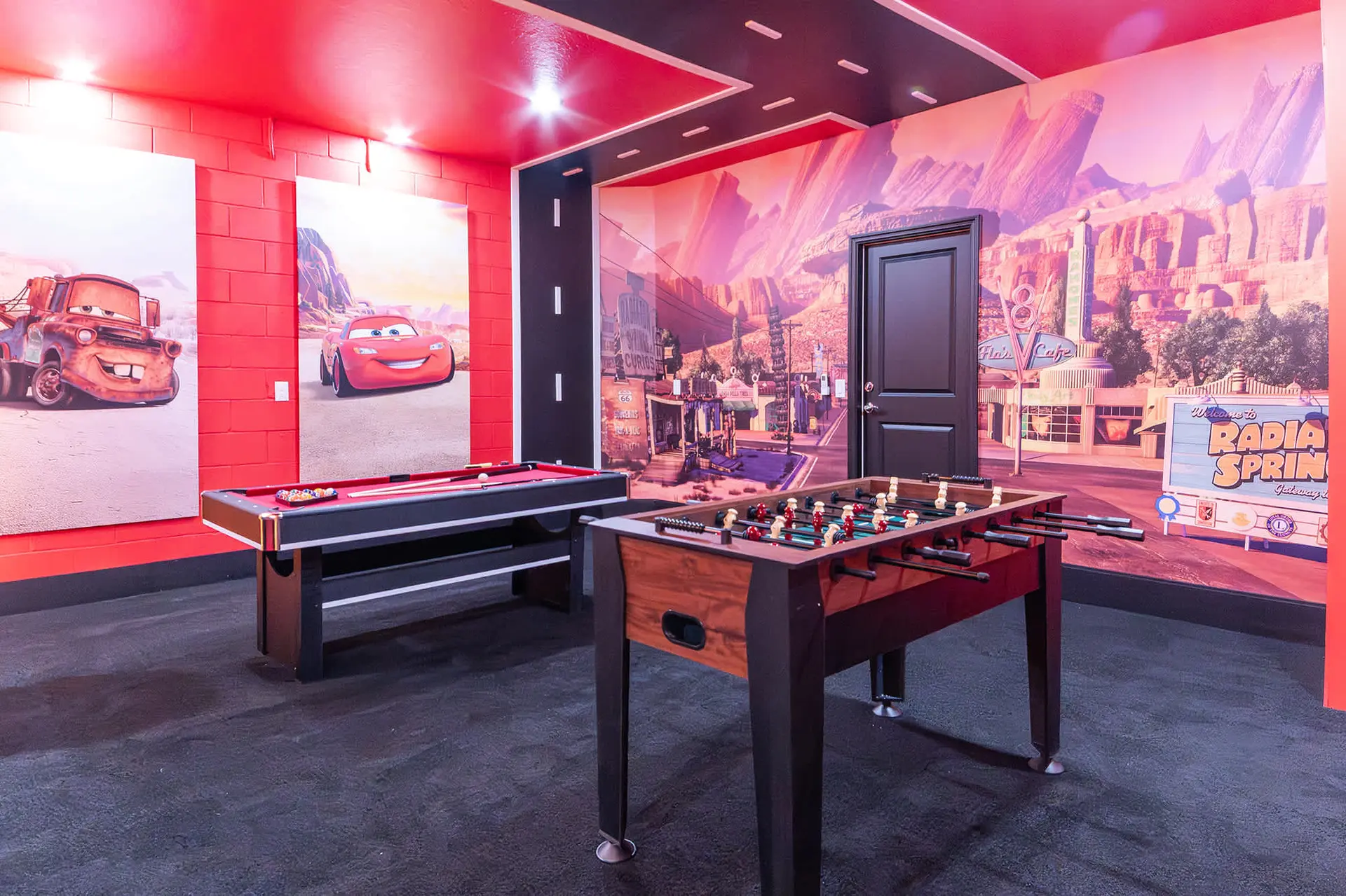 A playroom features a pool table and foosball table, with walls decorated with Cars movie characters