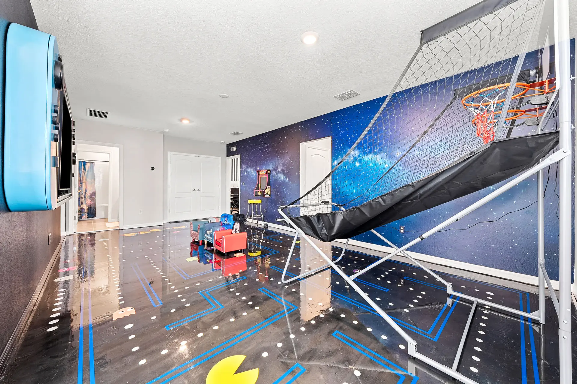 Game room with a starry night mural, Pac-Man floor, and basketball hoop.