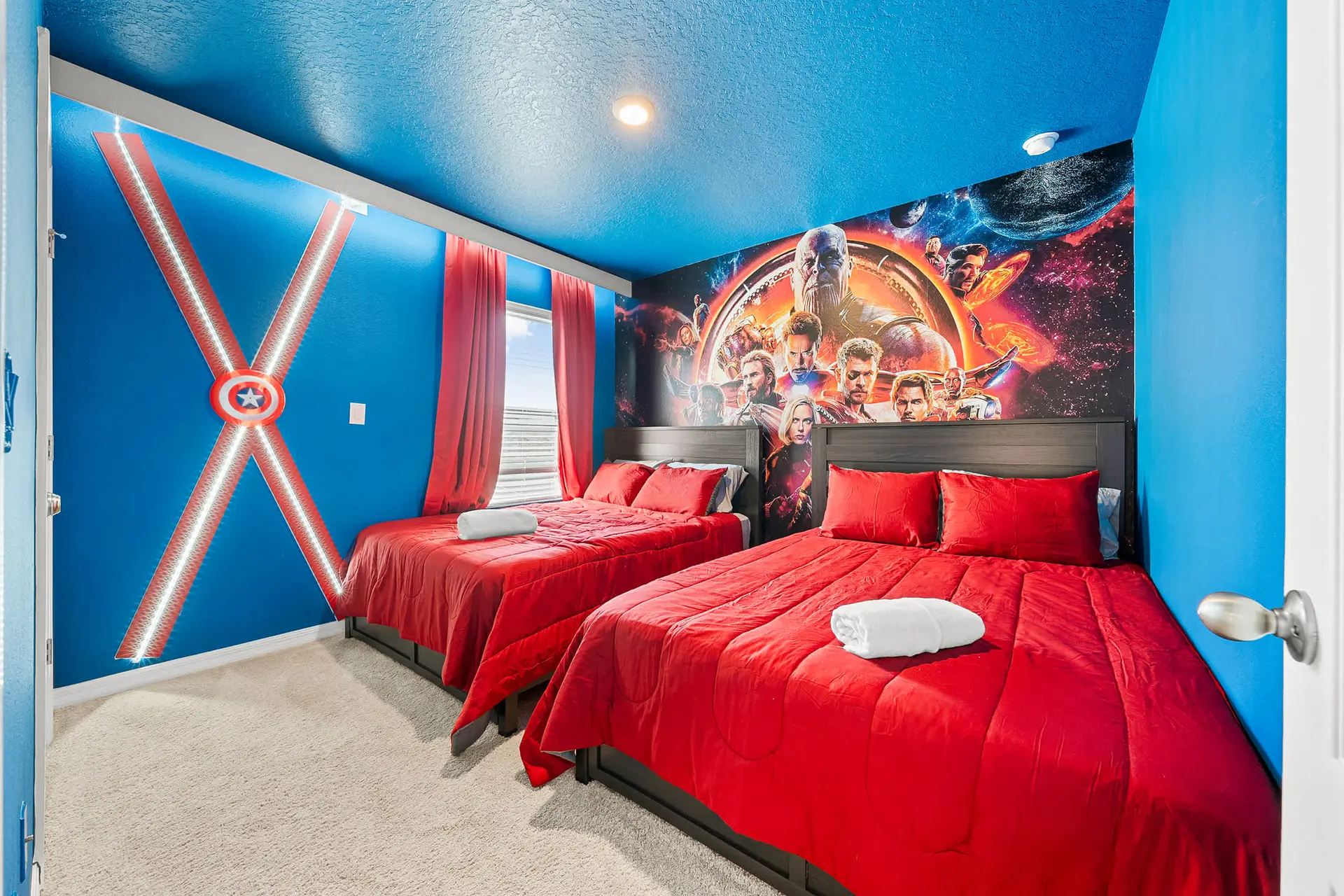 A bedroom with two beds, a Captain America mural, and a movie poster mural.
