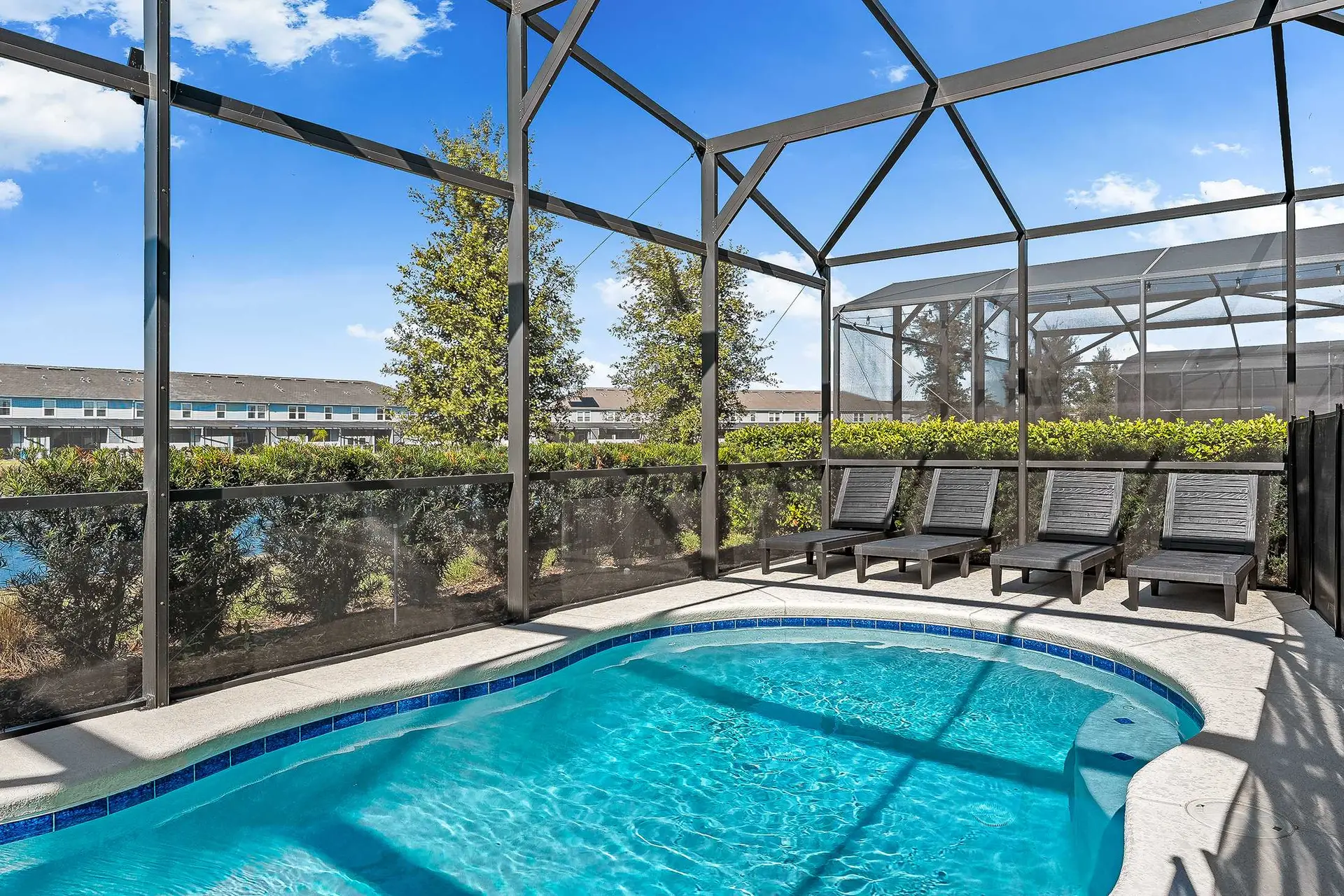 A screened-in pool with lounge chairs and lush greenery under a bright blue sky.