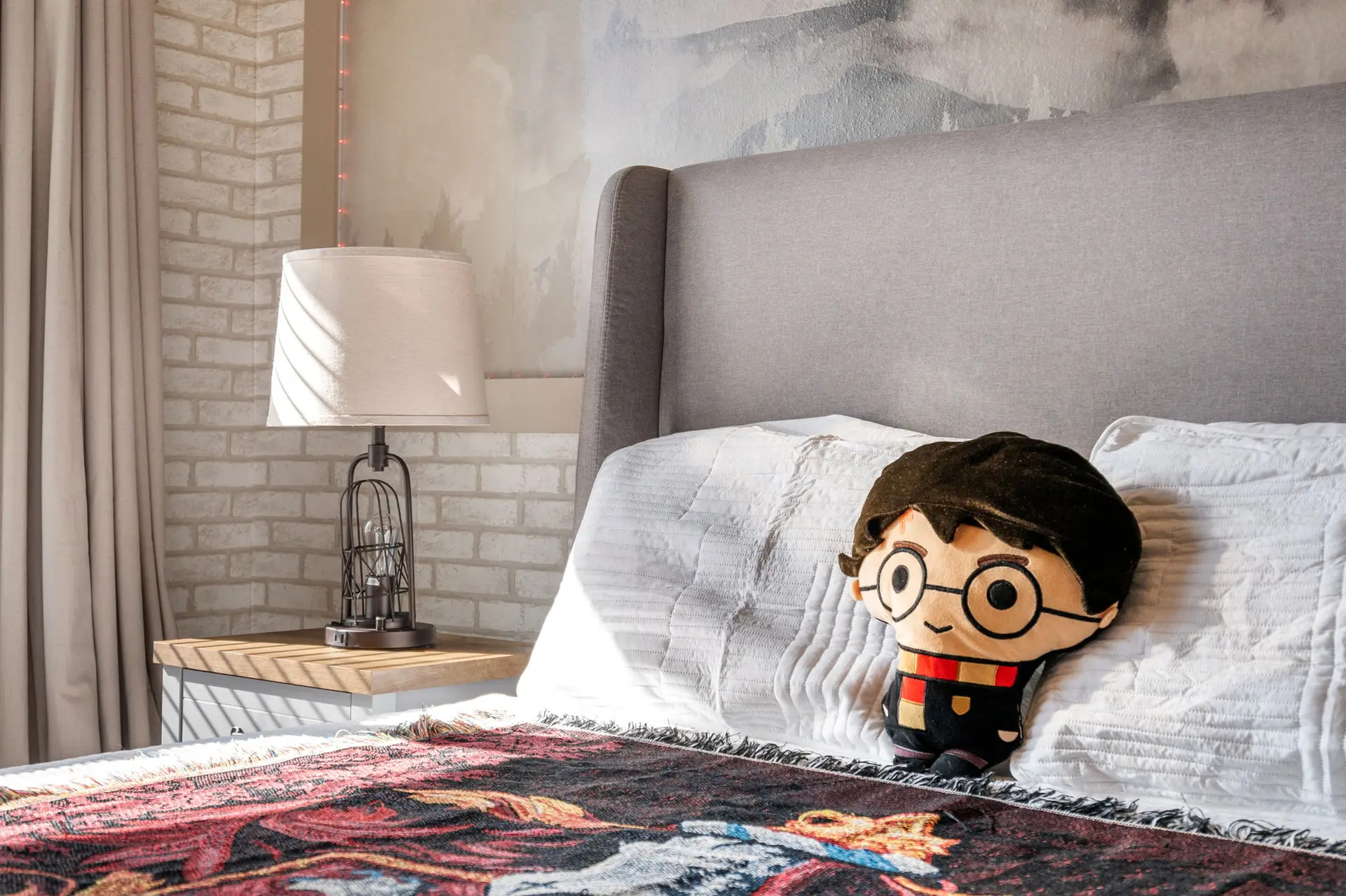 A Harry Potter plush toy sits on a bed next to pillows.