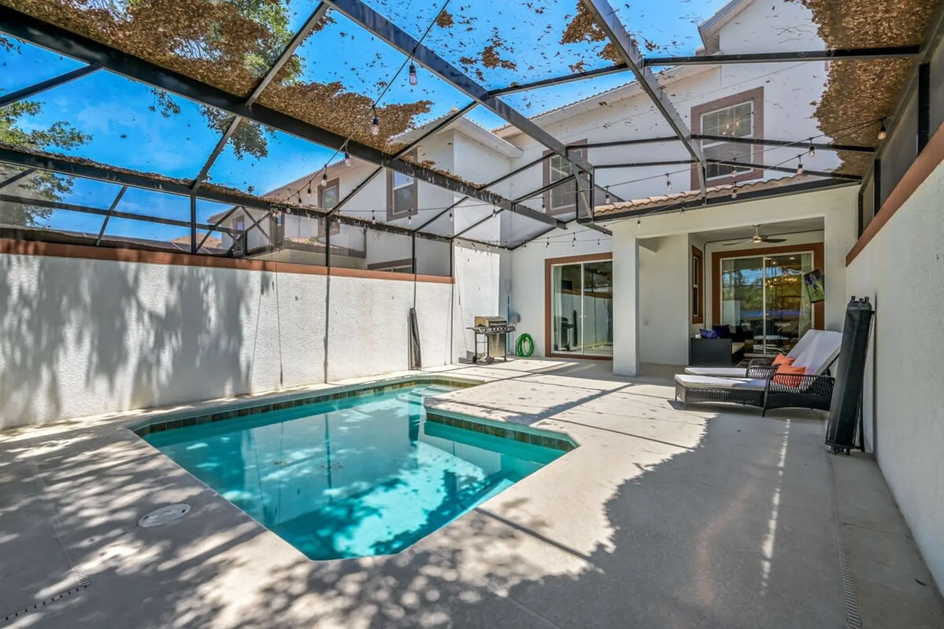 A backyard pool with lounge chairs under a screened-in patio.