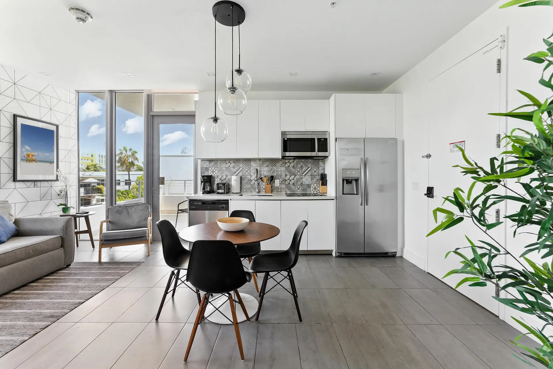 A modern kitchen and dining area with a gray sofa, round wooden table, and black chairs.