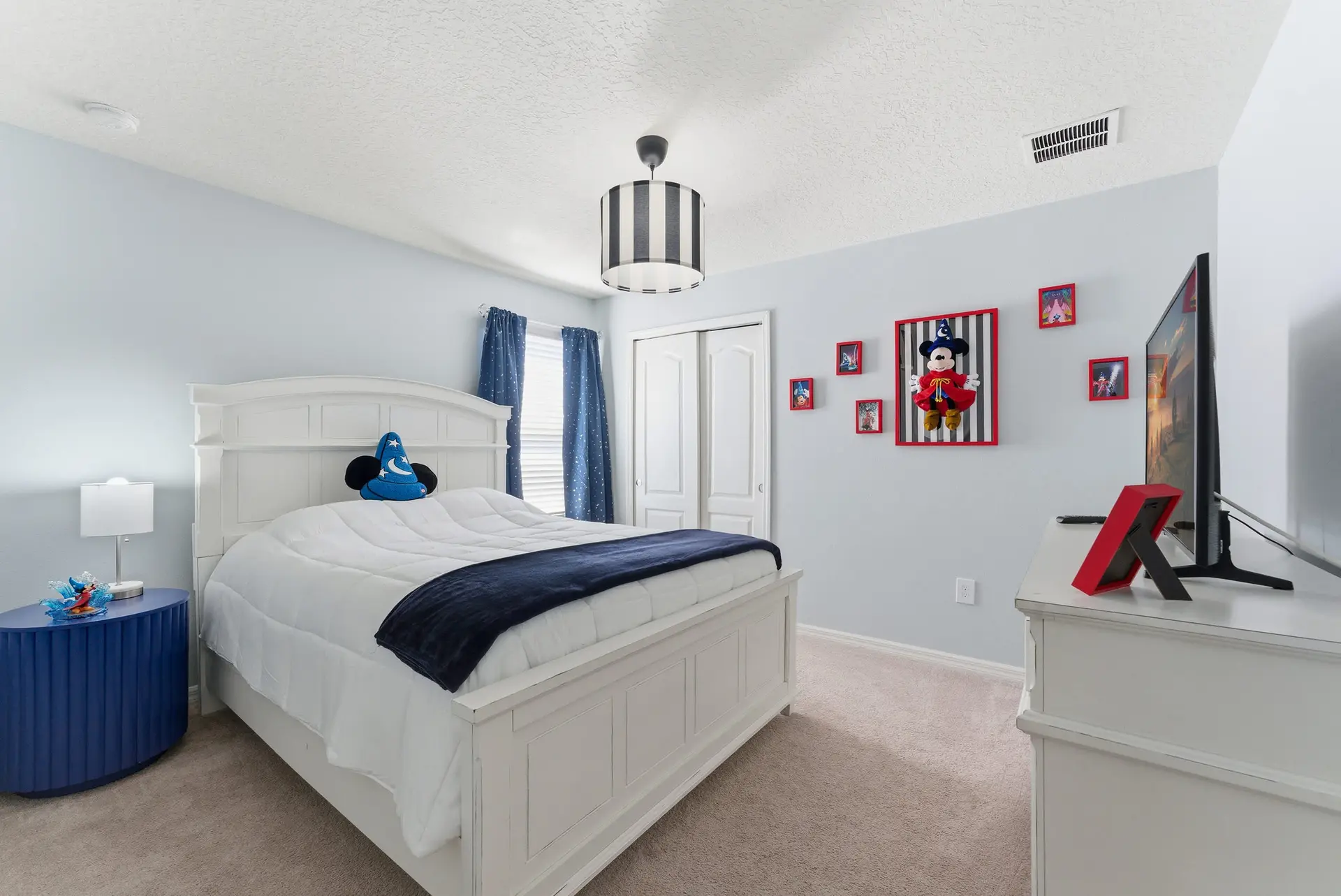 A Disney-themed bedroom with a white bed, blue curtains, and Mickey Mouse decor.