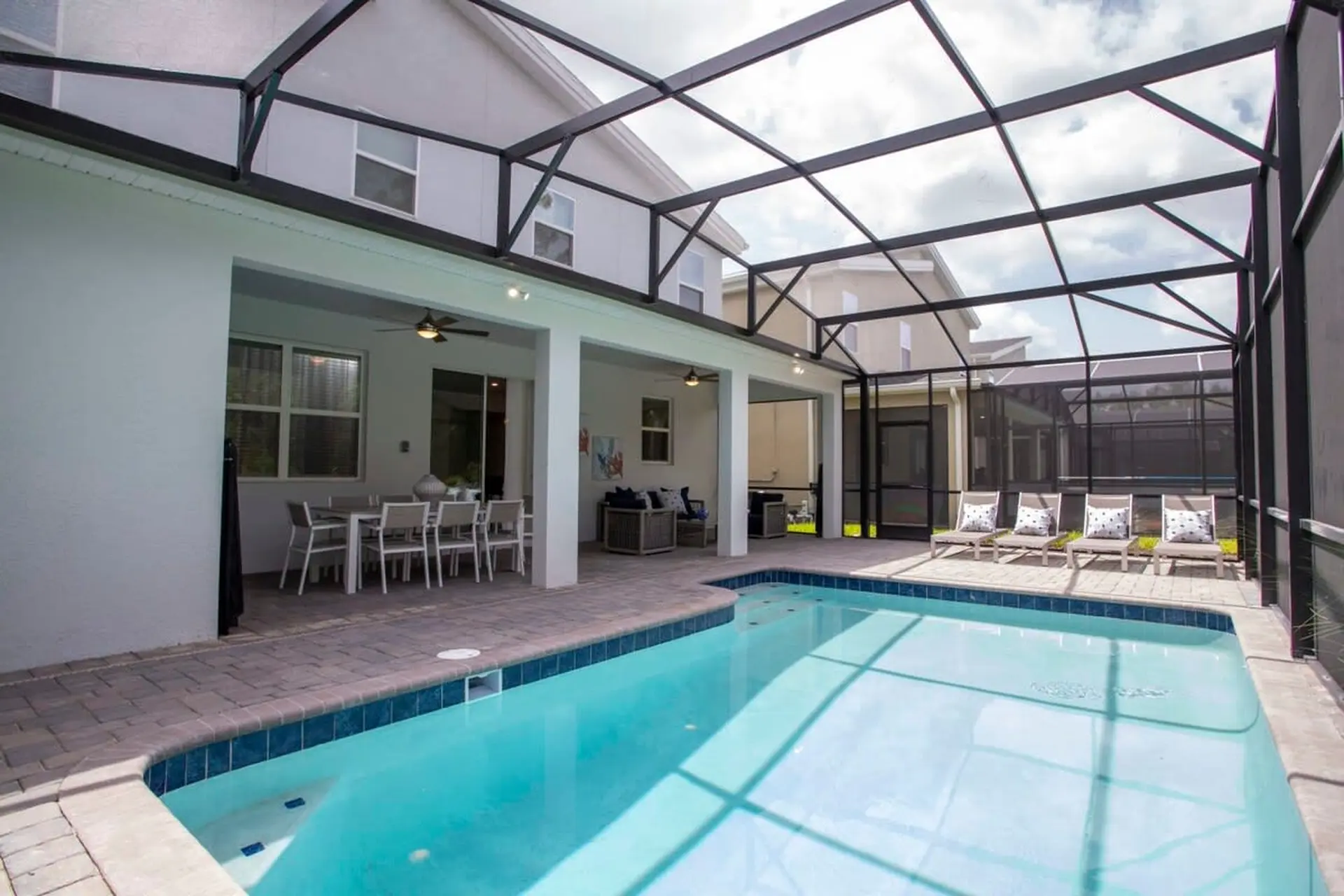 A screened-in patio with a pool, lounge chairs, and dining table.