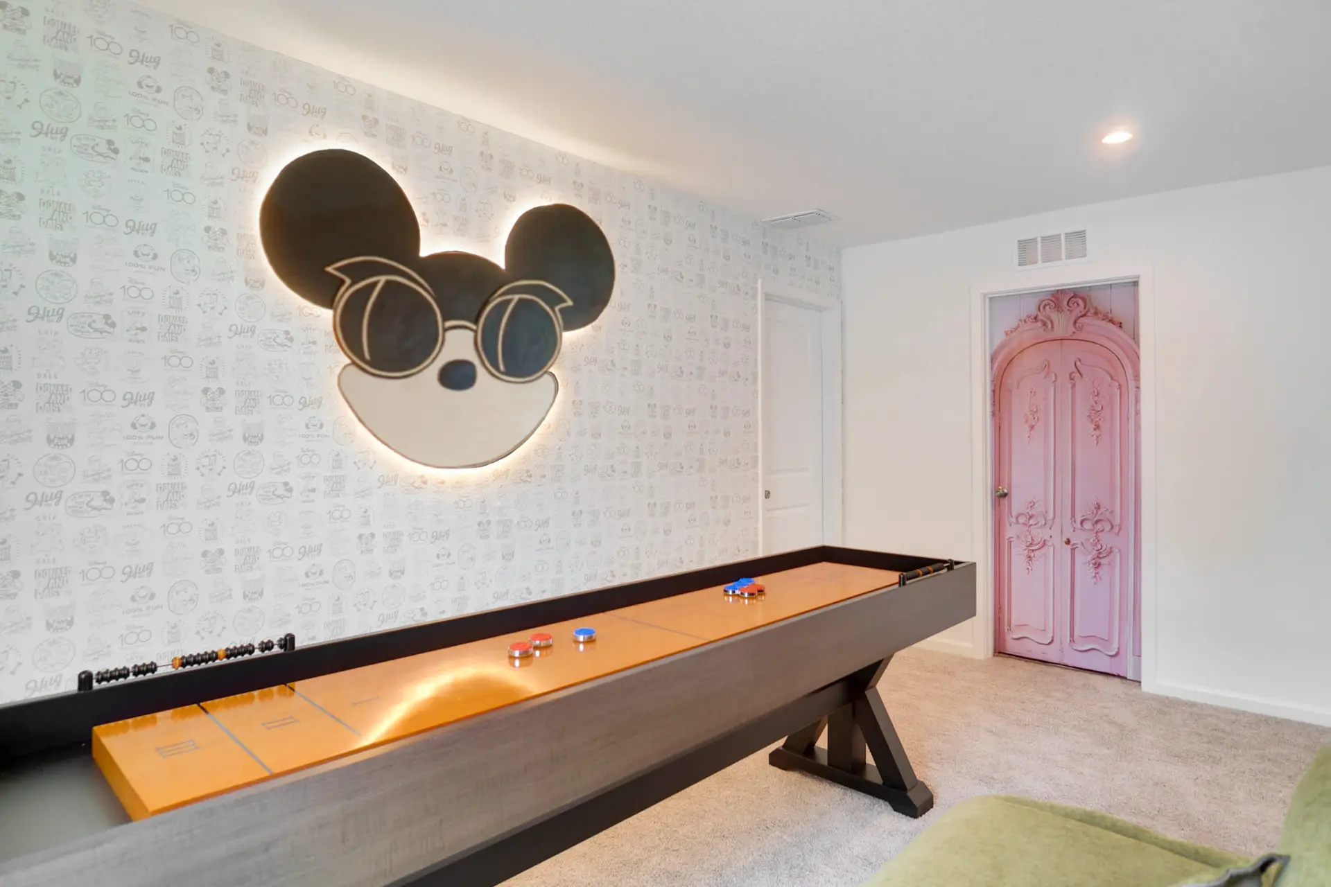A room with a shuffleboard, Mickey Mouse decor, and a pink door.