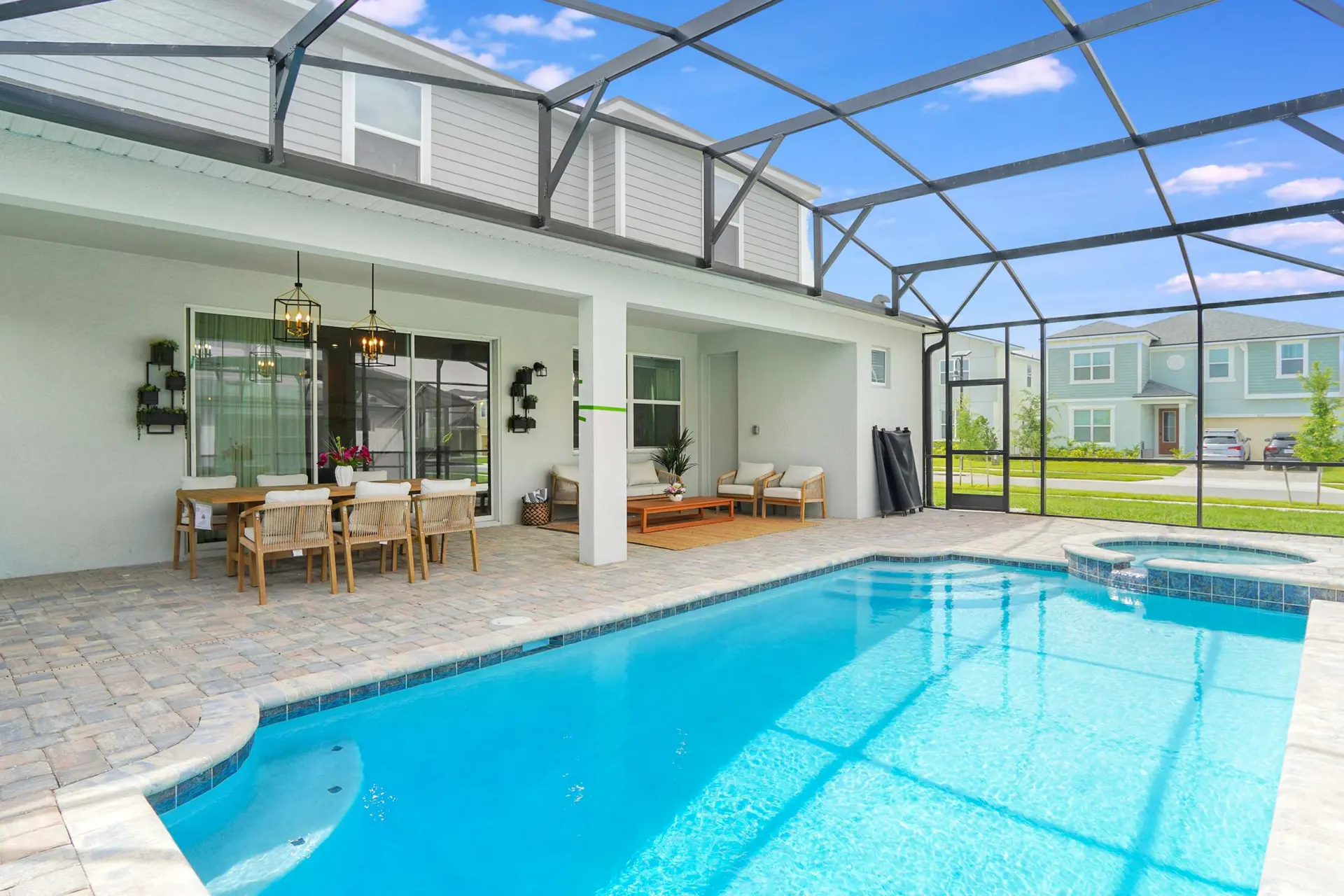 A screened-in patio with a pool and hot tub overlooks a light blue sky and neighboring houses.