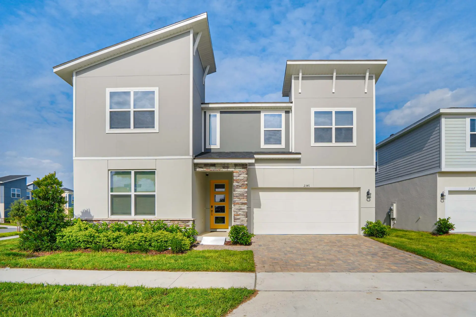 A modern two-story house with gray siding and a bright yellow door.