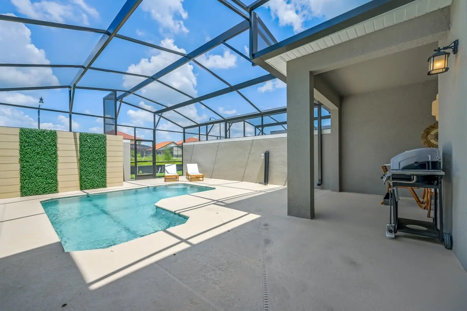 A modern backyard with a screened-in pool, lounge chairs, and a grill.