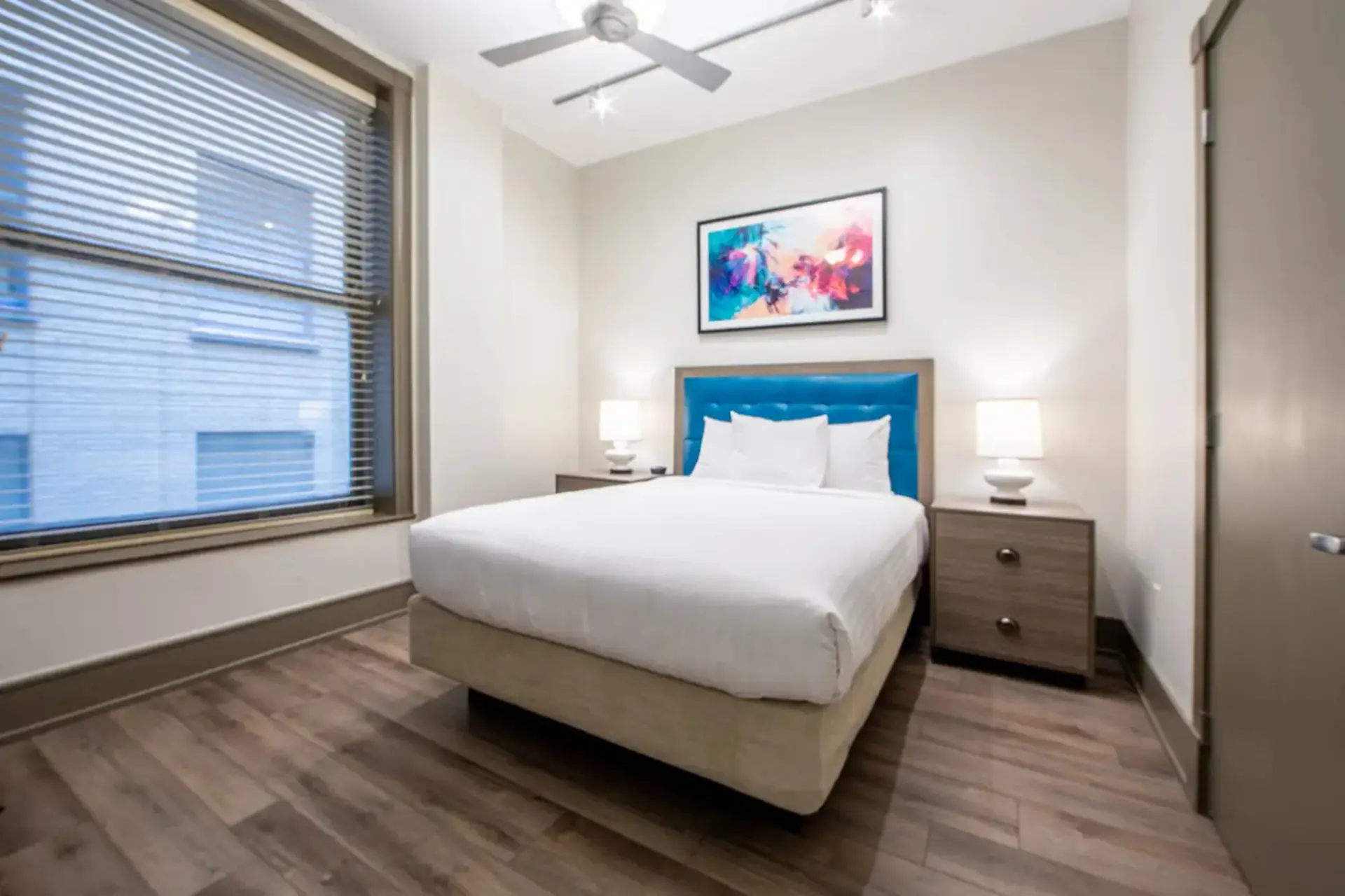 A modern hotel bedroom with a queen bed, nightstands, a large window, and ceiling fan.