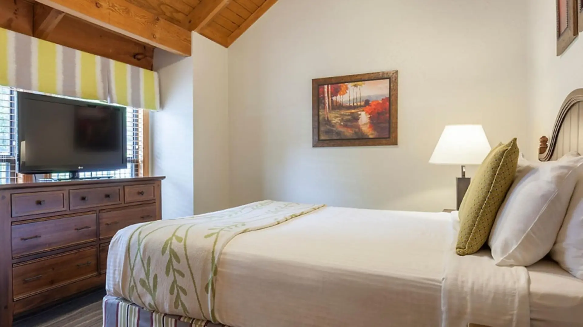 A bedroom with a TV, dresser, bed, and artwork.