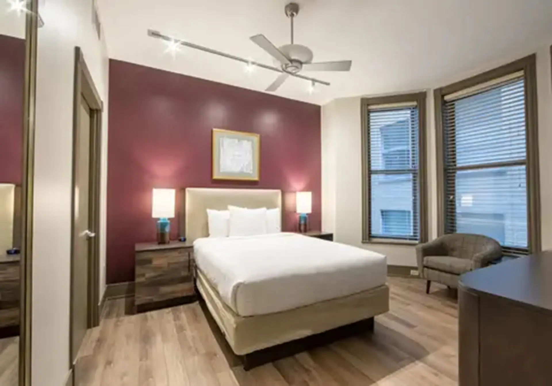 A bedroom with a king-size bed, bedside tables, a ceiling fan, and two windows.