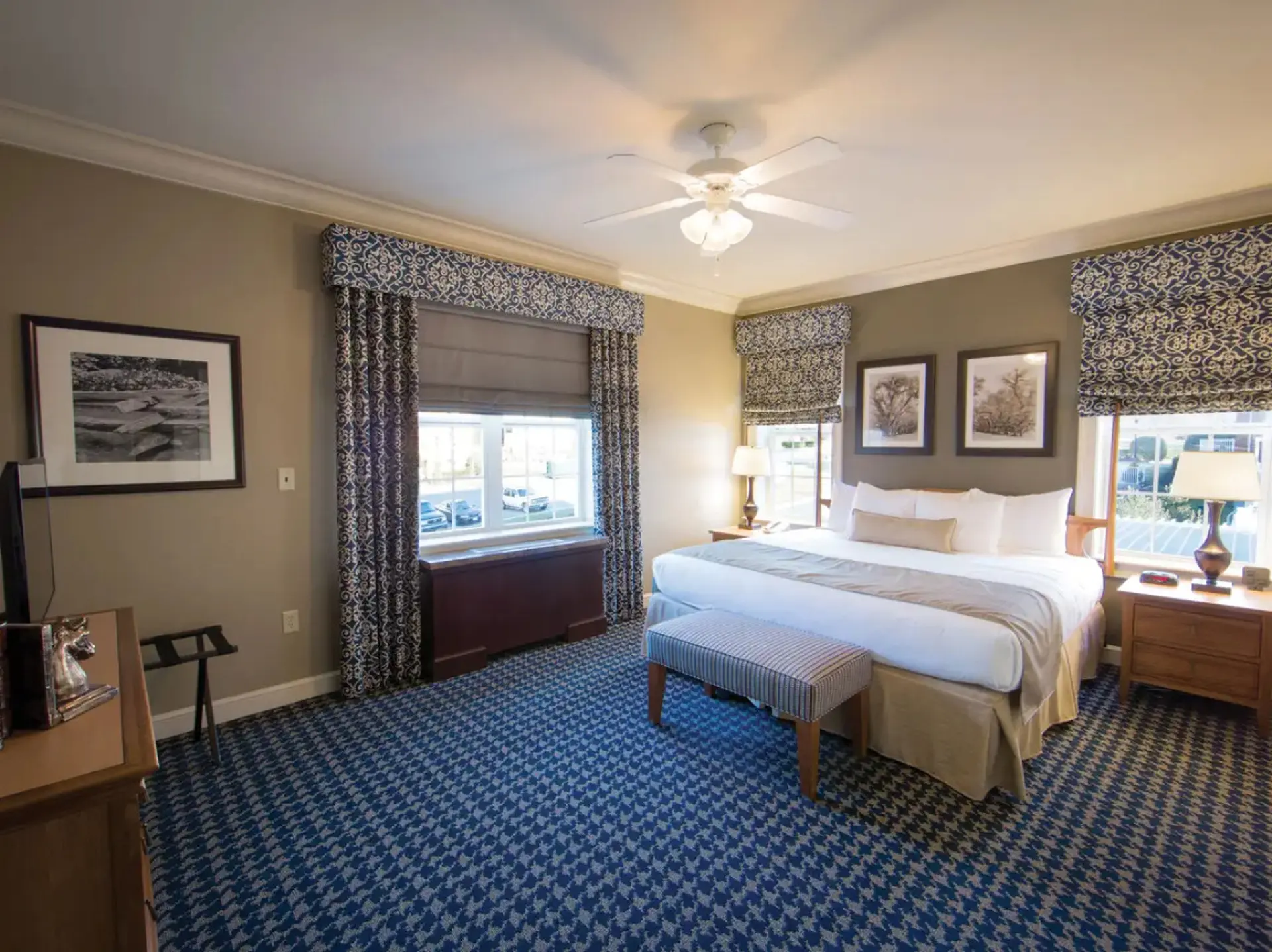 A king-size bed with crisp white linens sits in a hotel room with a blue patterned carpet.
