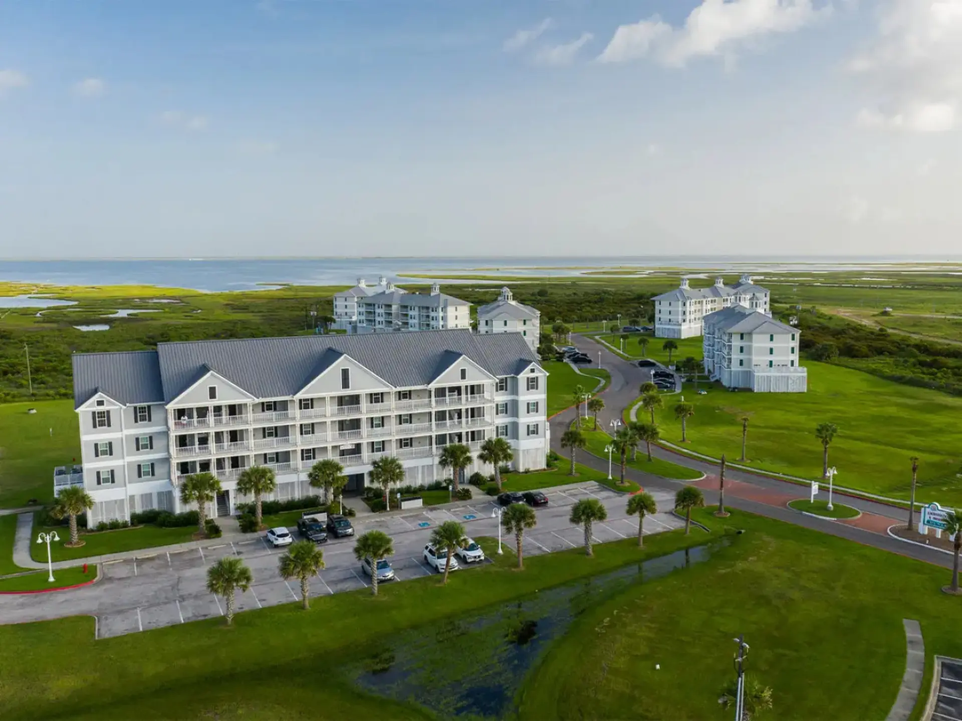 Resort buildings on a grassy hill overlooking marshland and the ocean.