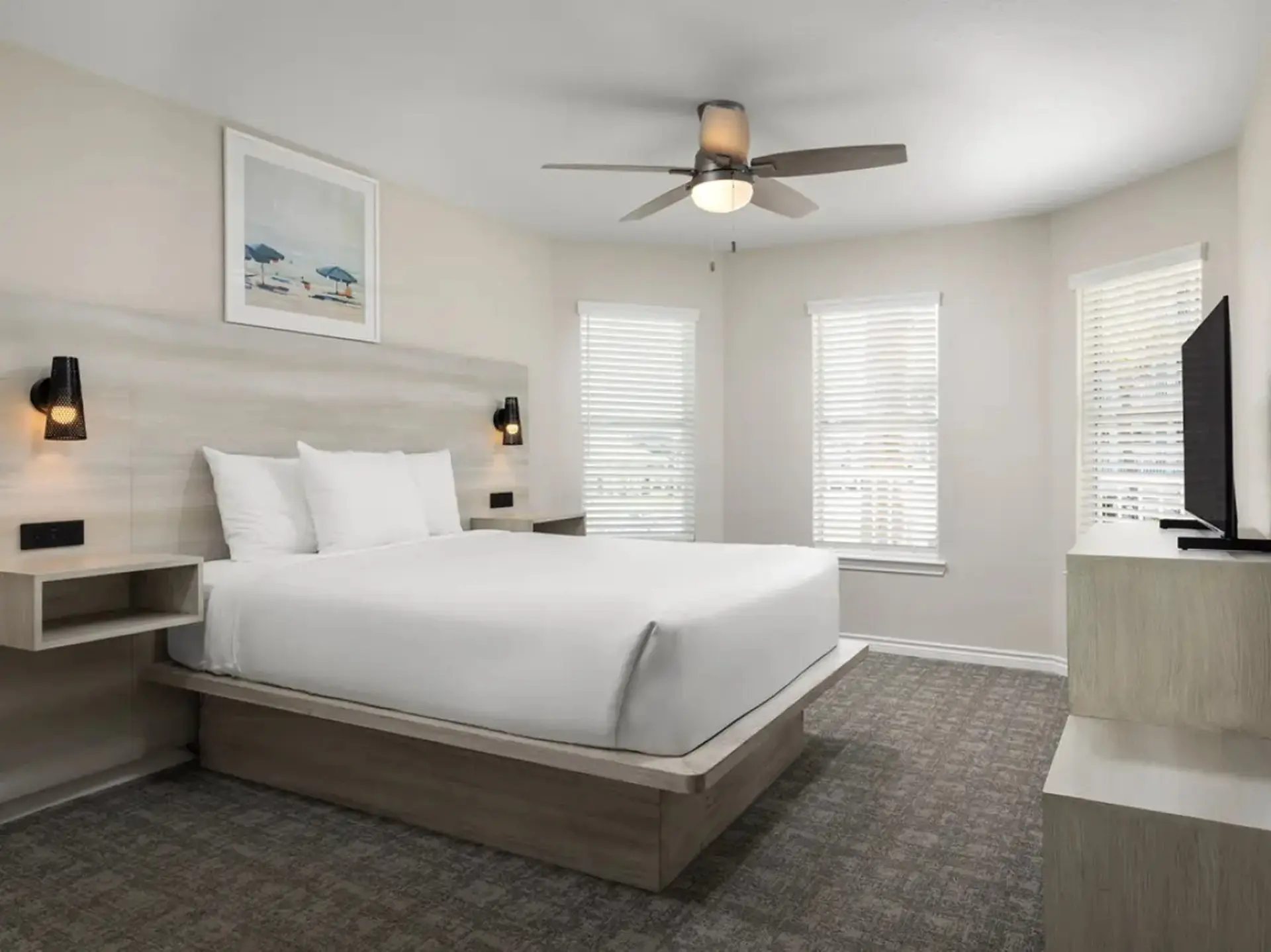 A bedroom with a king-sized bed, ceiling fan, and a television.