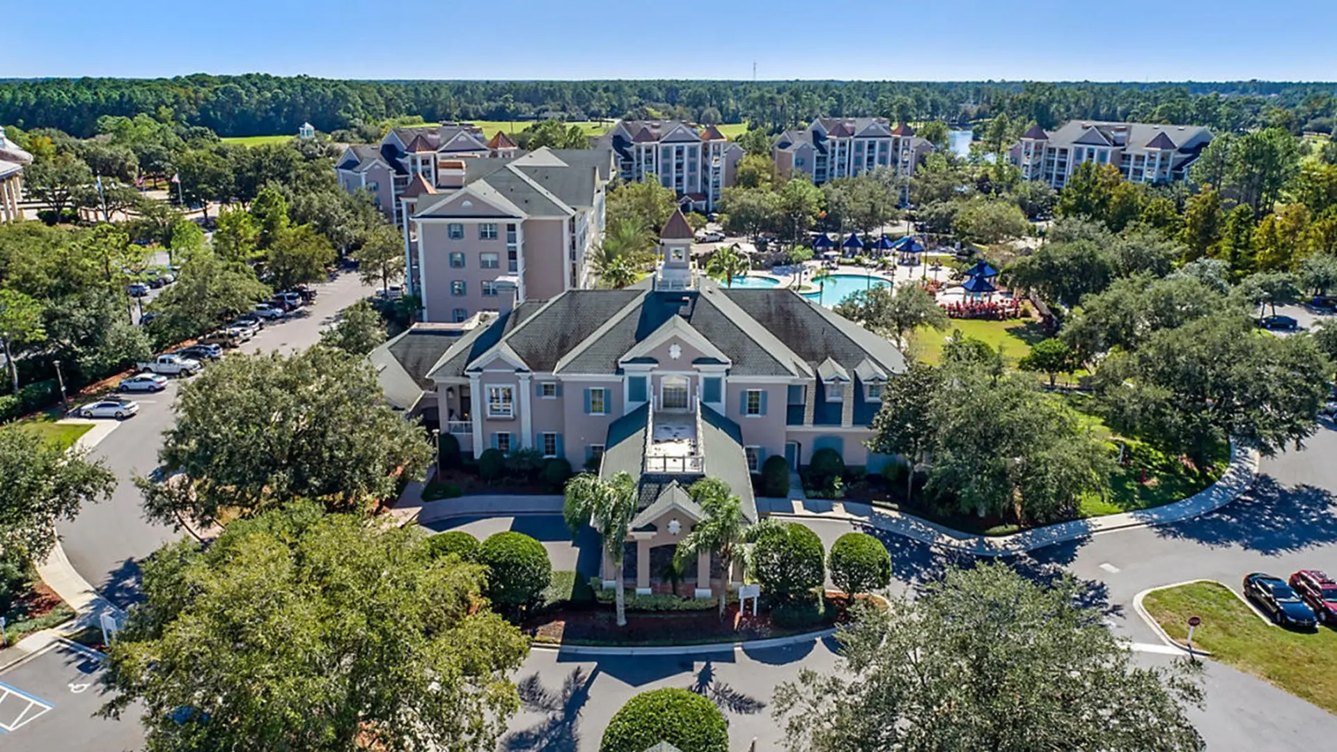 Resort with a central building, pool, and surrounding trees and apartment complexes.