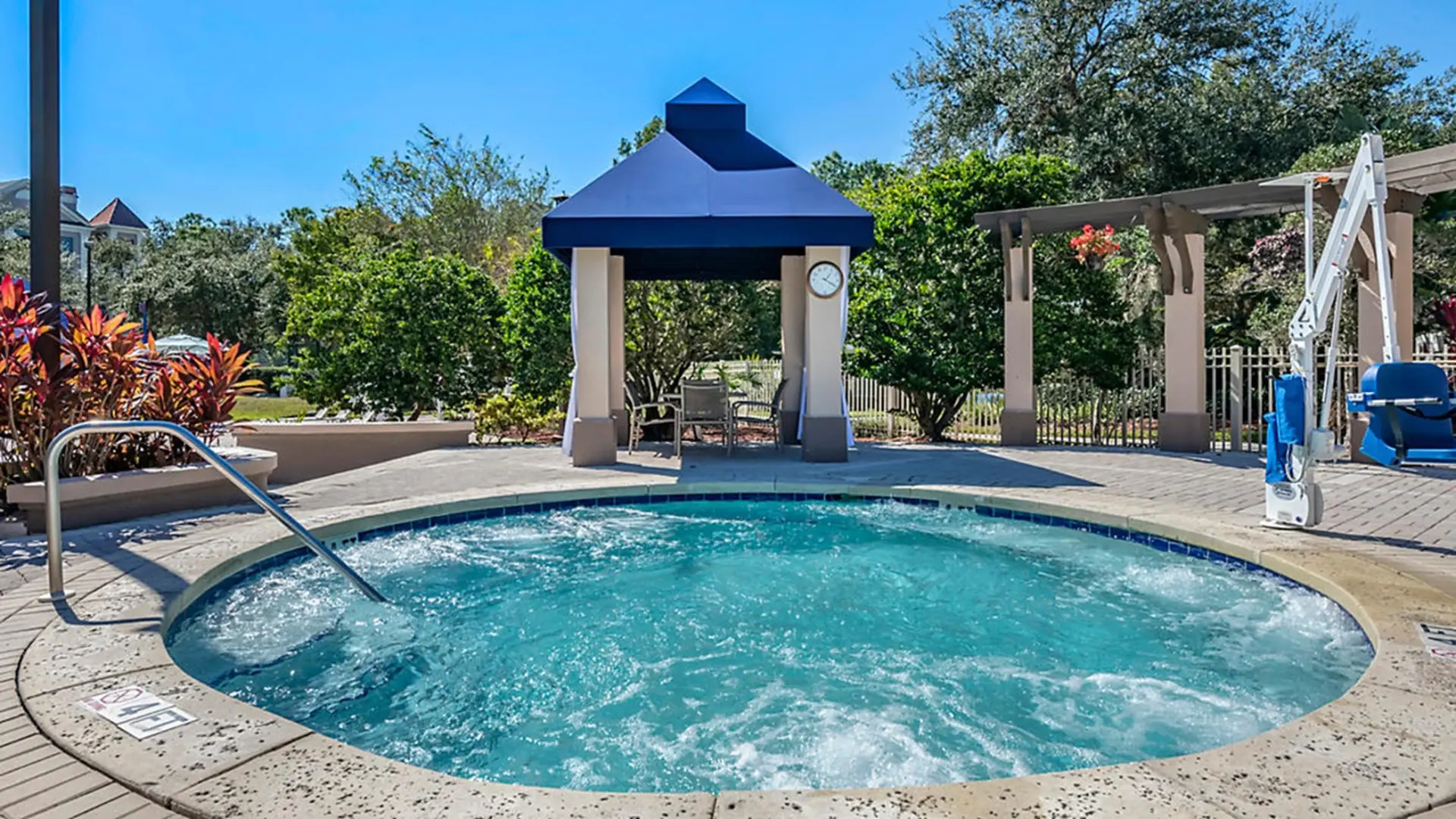 Outdoor spa with bubbling turquoise water, seating under a blue gazebo, and a pool lift.