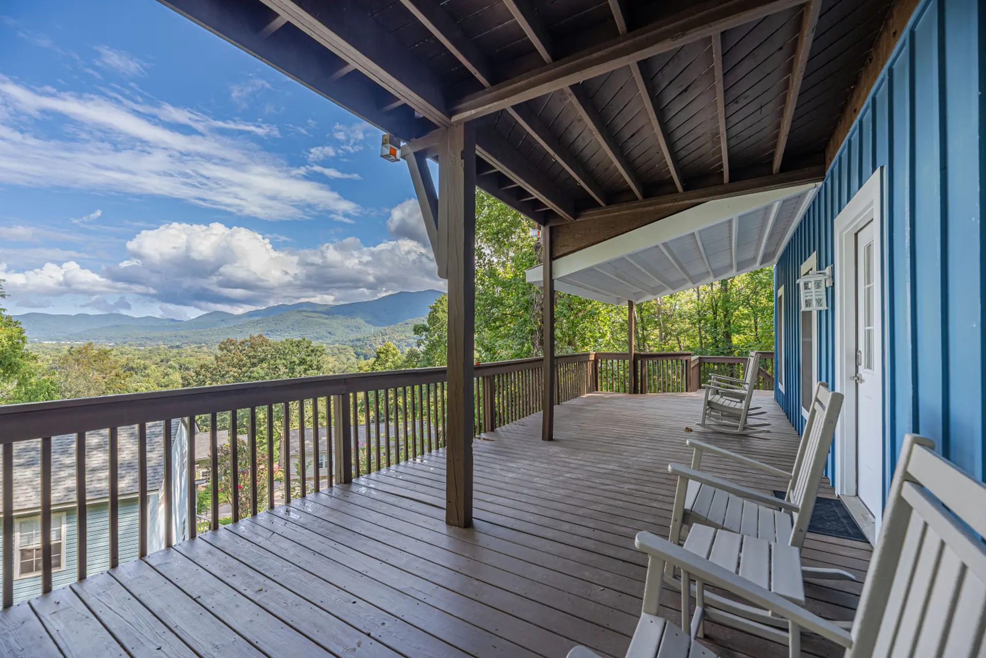 Wooden porch with rocking chairs overlooking mountains and trees.