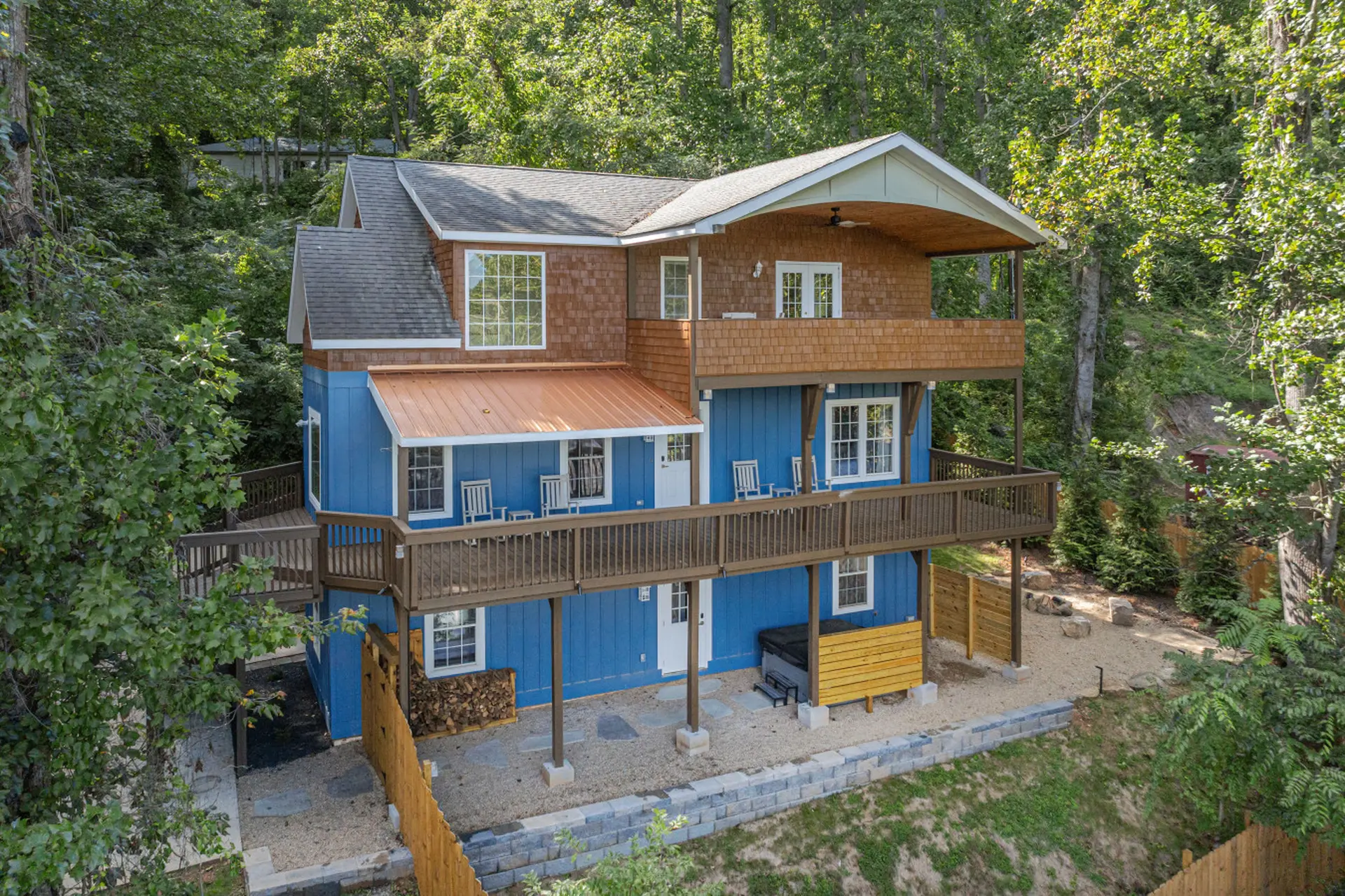 Blue wooden house with multiple decks surrounded by trees.