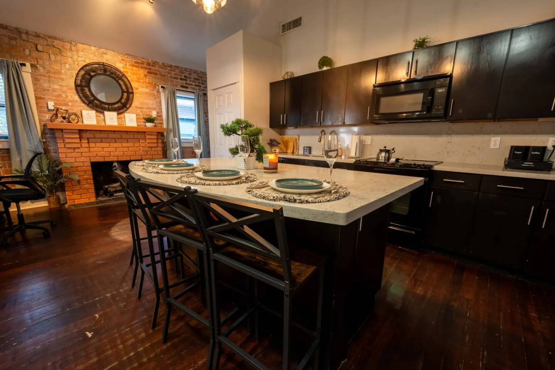 A modern kitchen with dark cabinetry, an island with stools, and a brick fireplace.