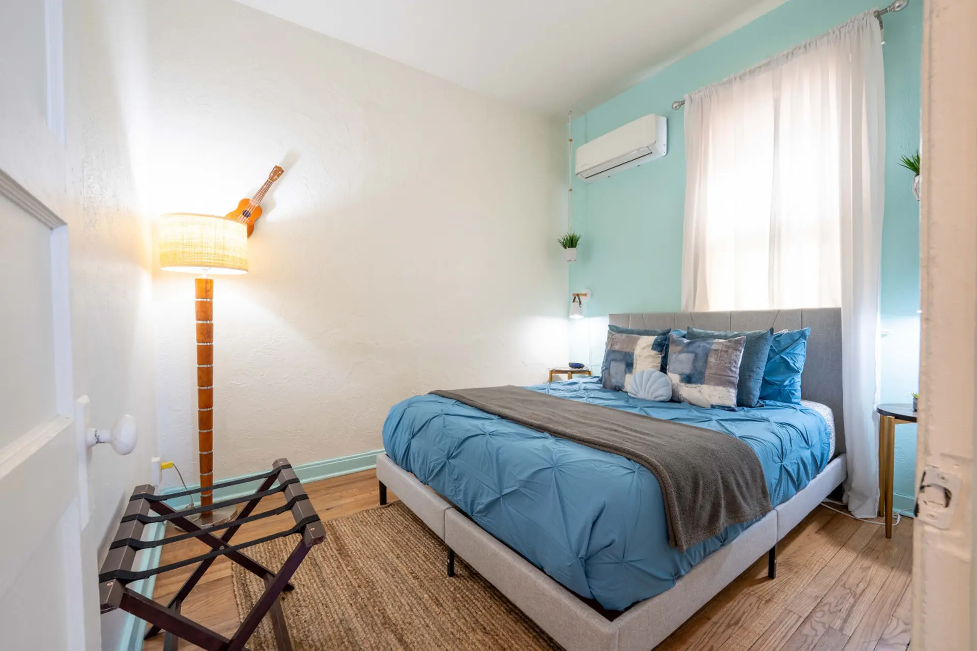 A bedroom with a king-size bed, blue comforter, and a ukulele on a lamp.