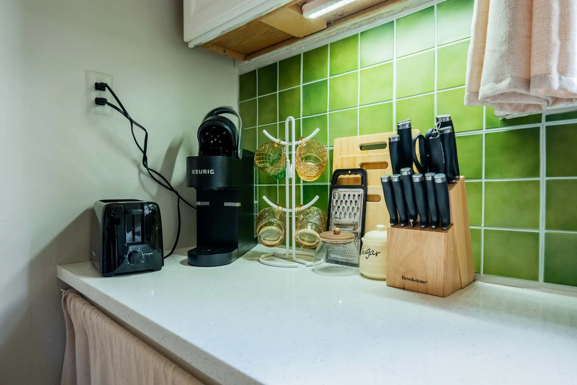 Kitchen counter with Keurig, toaster, mugs, knives, grater, and sugar dish.